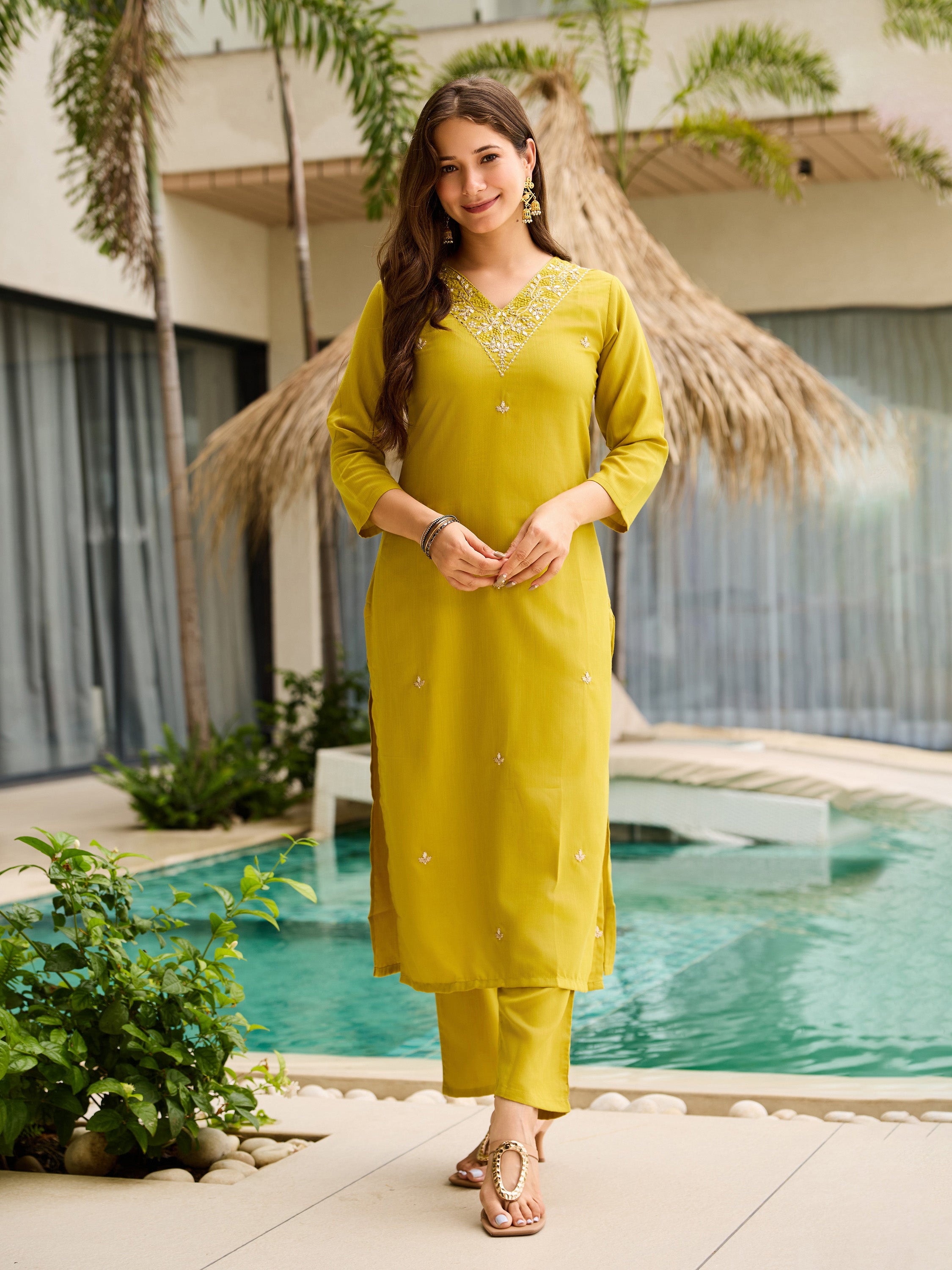 Woman in a yellow traditional kurta set outfit standing by a pool with greenery in the background