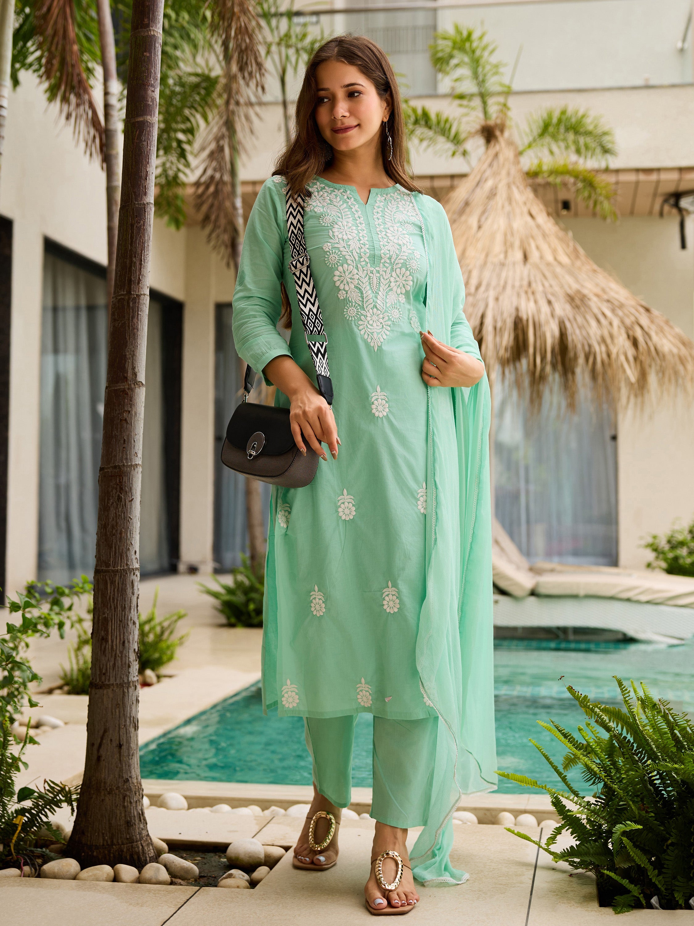 Woman in a mint green traditional kurta set with dupatta standing by a poolside.