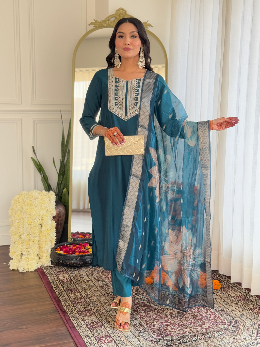 Woman in a blue traditional outfit with a floral arrangement and mirror in the background