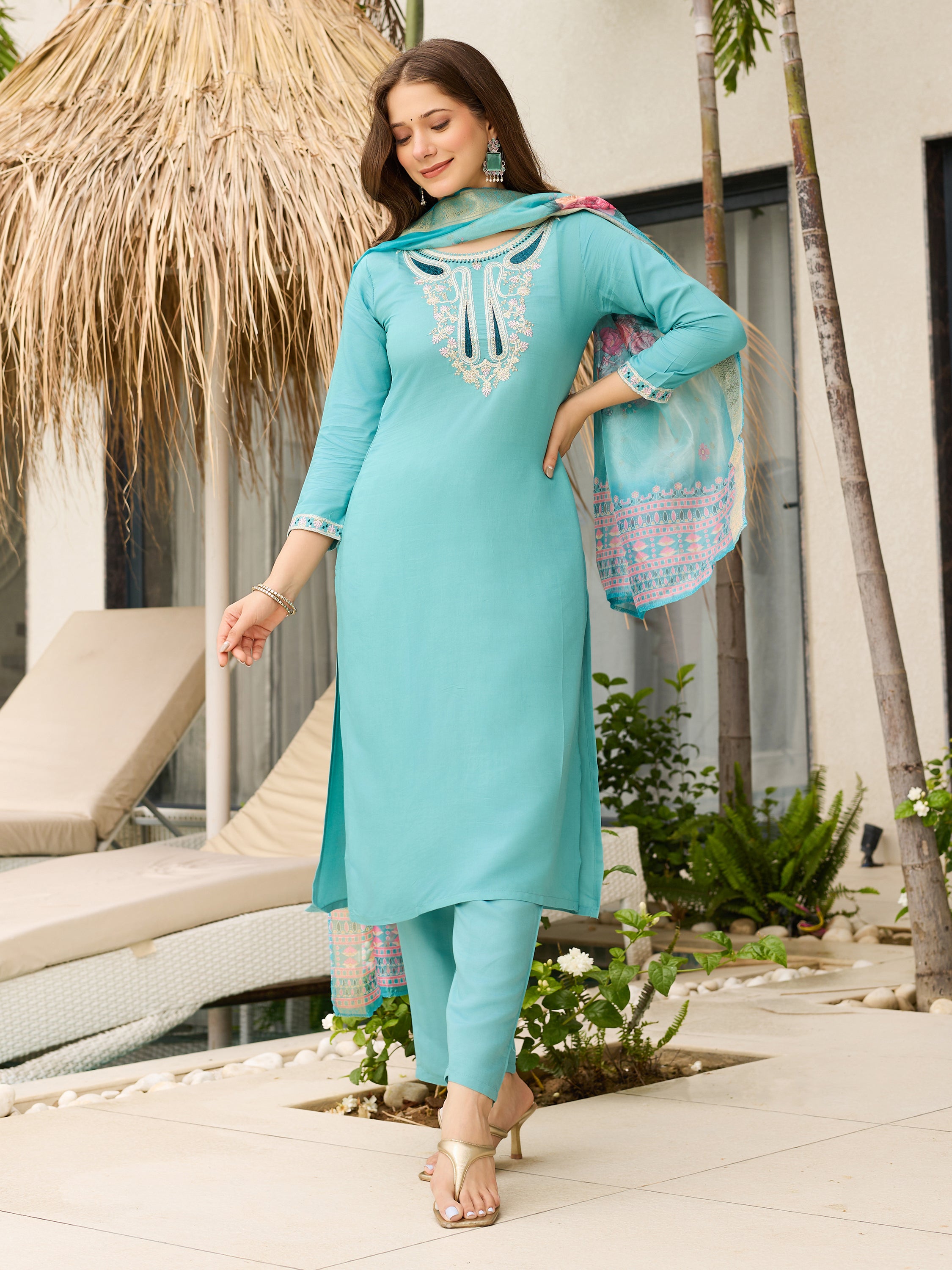 Woman in a sky blue kurta set with dupatta outfit standing outdoors near a poolside area.
