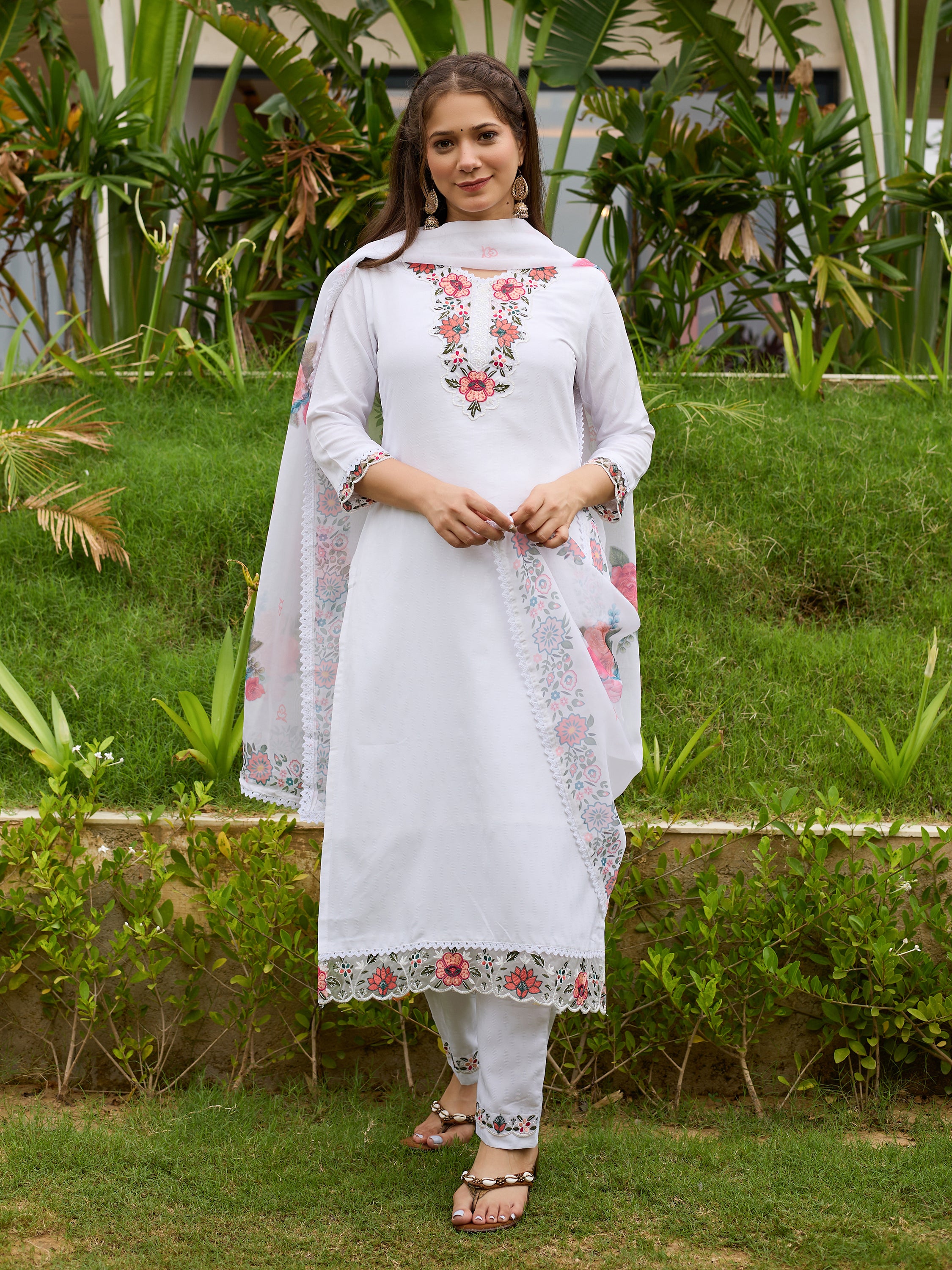 Woman wearing a white embroidered outfit standing in a garden.