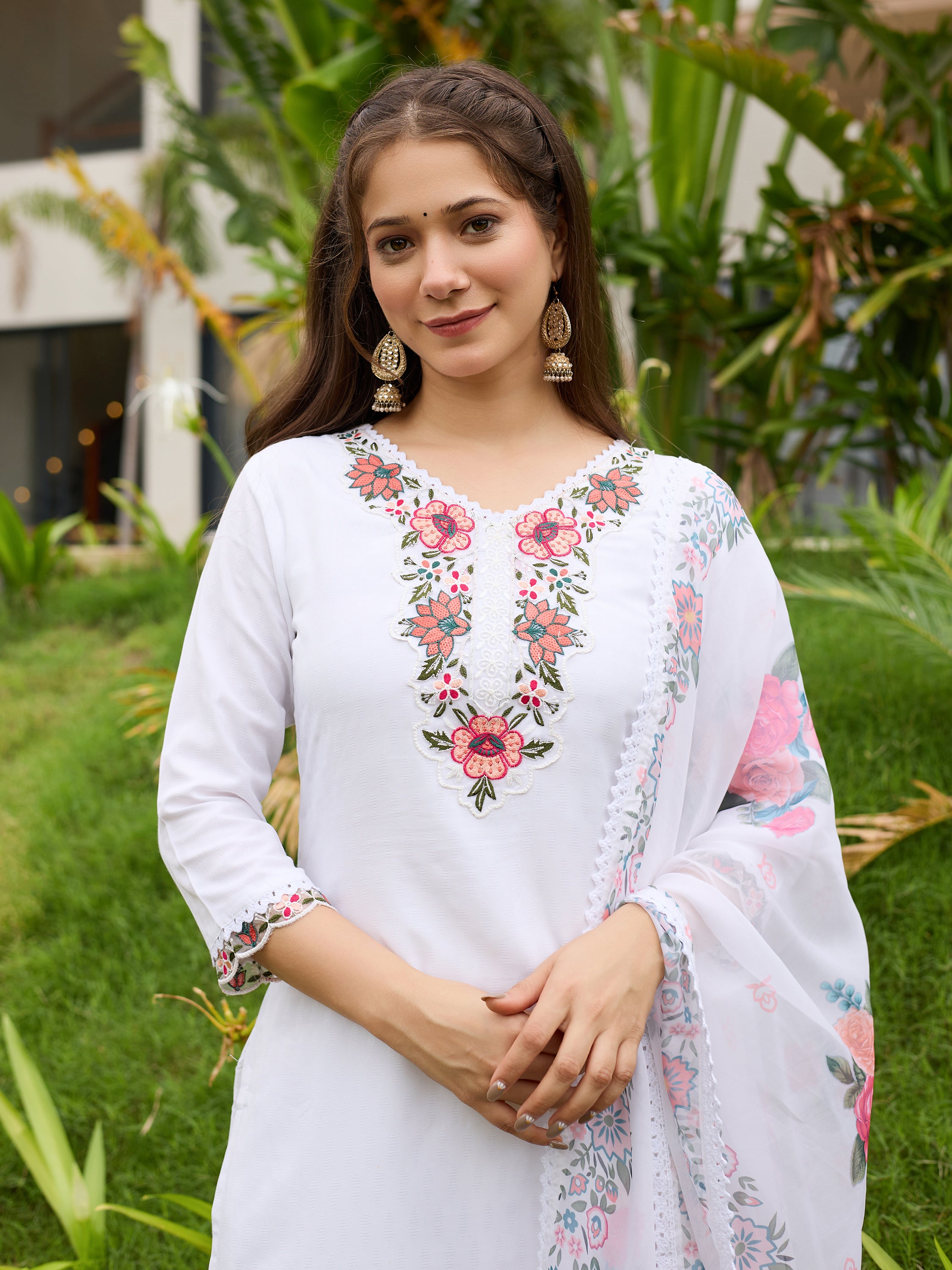 Woman wearing a white embroidered outfit with a floral pattern in an outdoor setting.