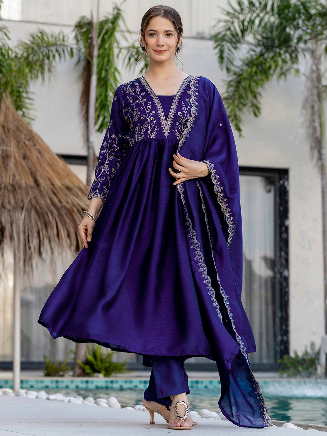 Woman wearing a purple kurta set with embroidered outfit standing by a pool with greenery in the background