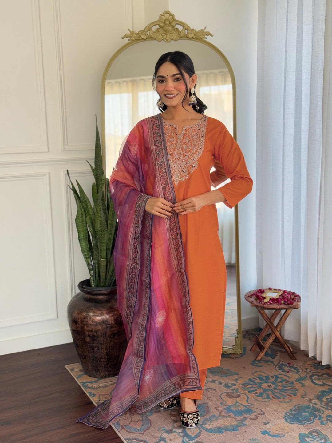 Woman in an orange outfit with a purple dupatta standing in front of a mirror.