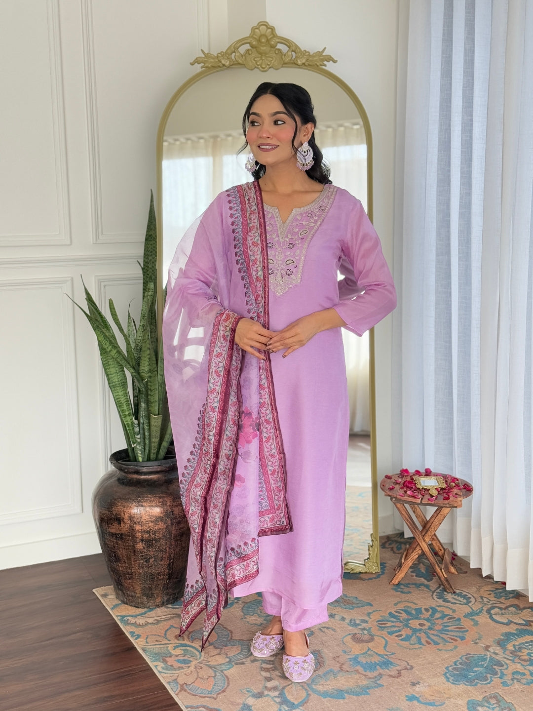 Woman in a pink traditional outfit standing in a room with a mirror and plant.
