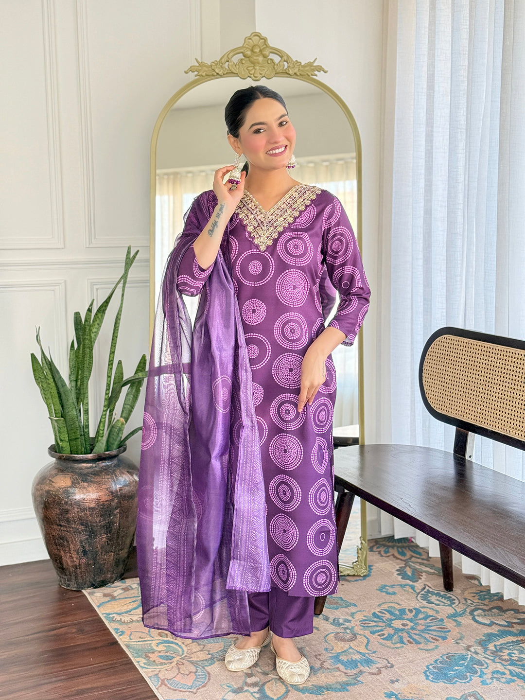 Woman in a purple traditional outfit standing in a room with a mirror and plant.