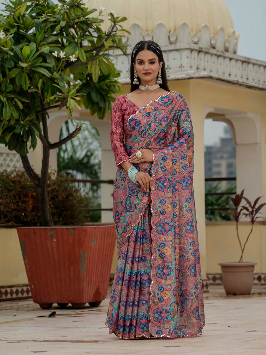 A woman in a dusty rose floral ready-to-wear saree stands outdoors with architectural elements in the background.