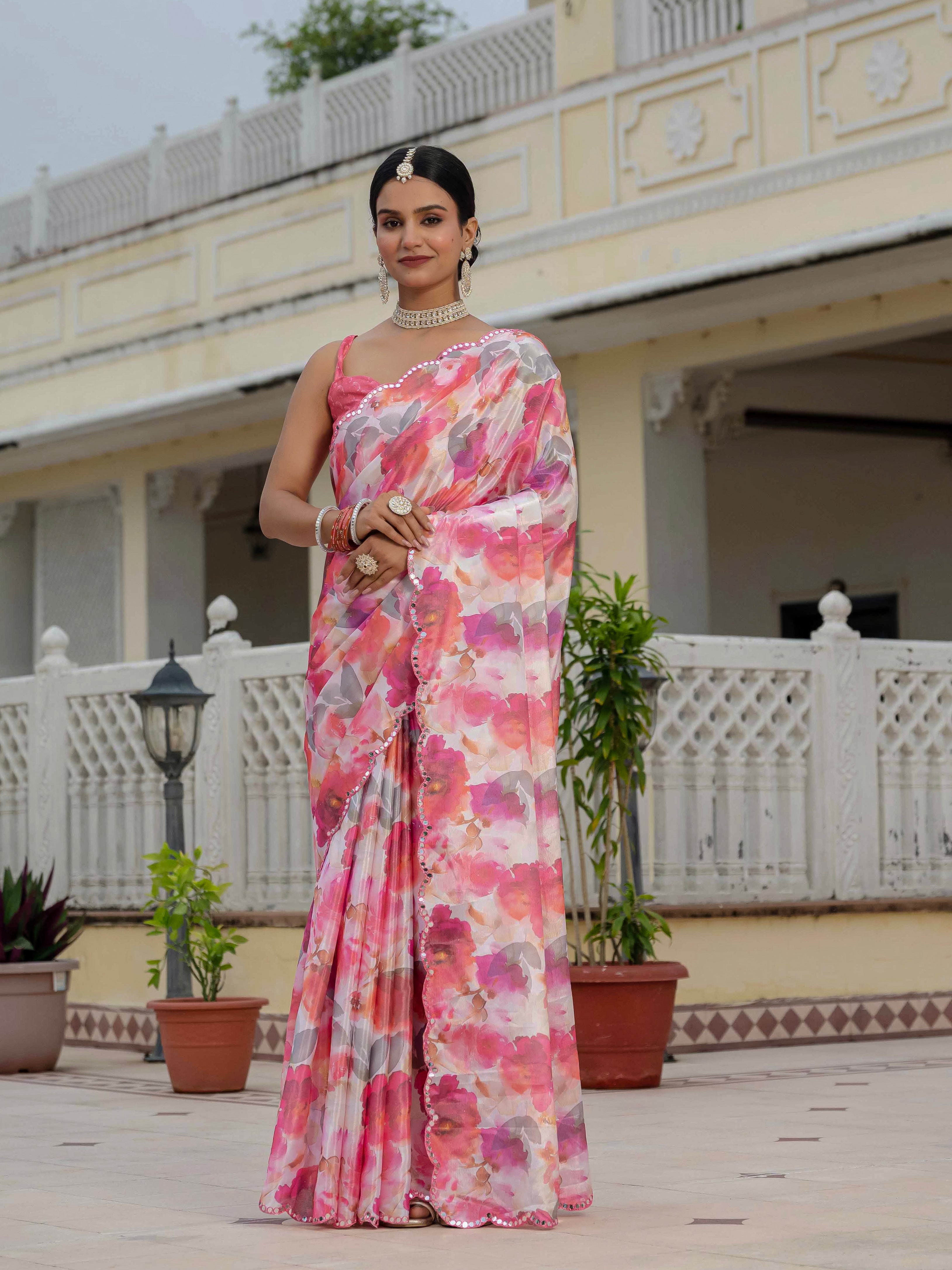 A woman wearing a soft blush pink ready-to-wear floral saree stands before a traditional building.