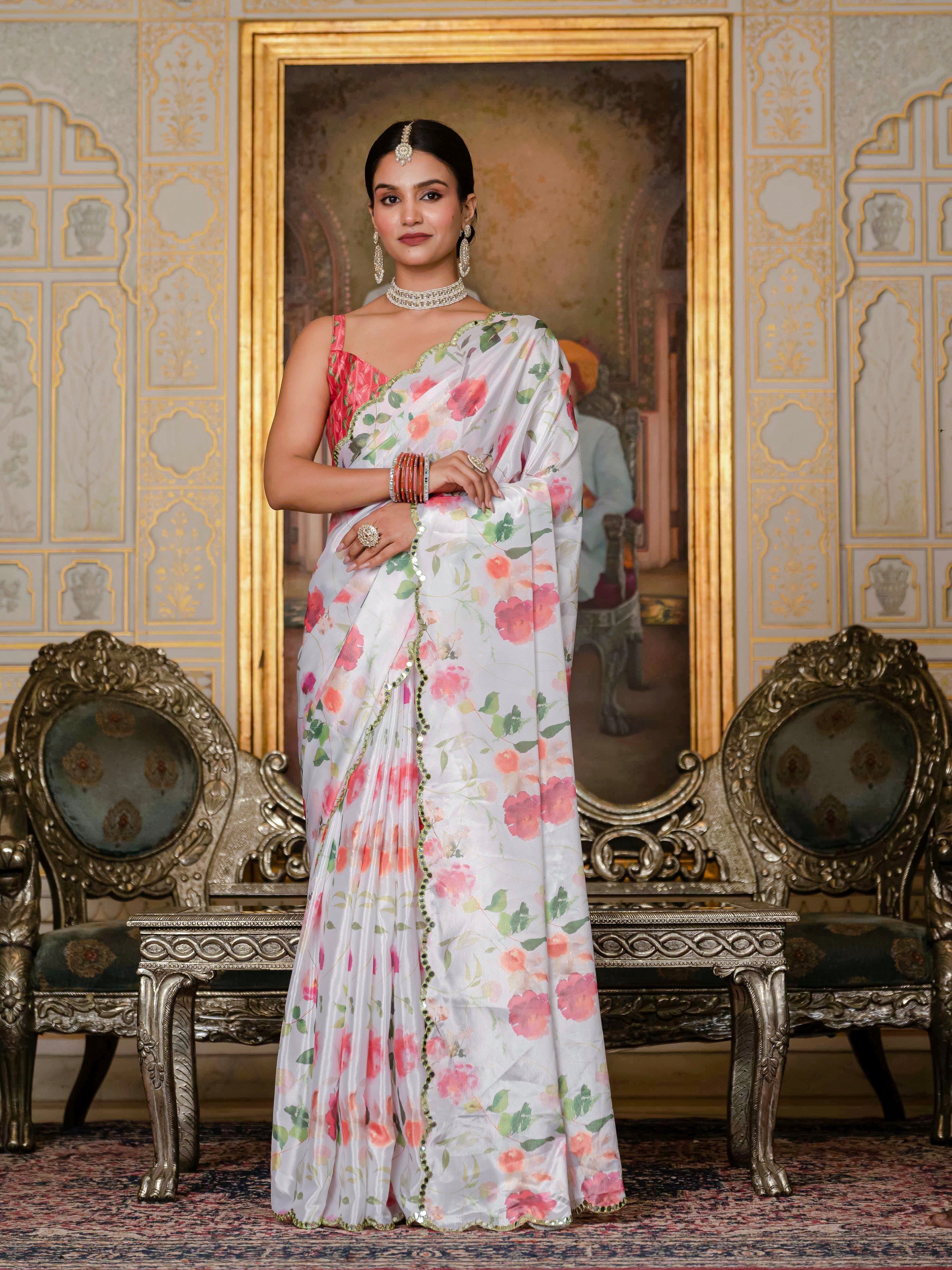 A woman wearing an off-white ready-to-wear floral saree stands in an ornate room with chairs and a mirror.