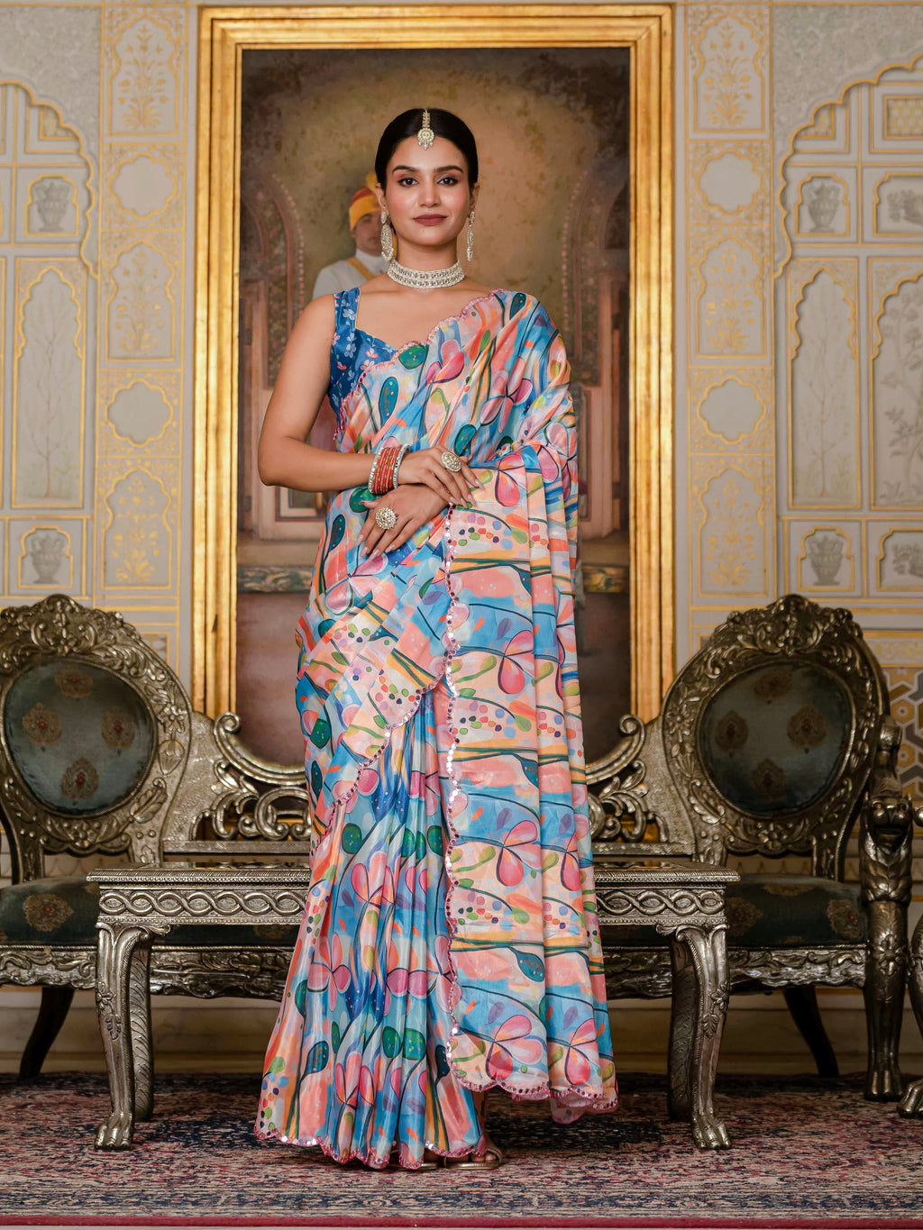 A woman in a soft sky blue ready-to-wear saree stands in an ornate room with decorative chairs.