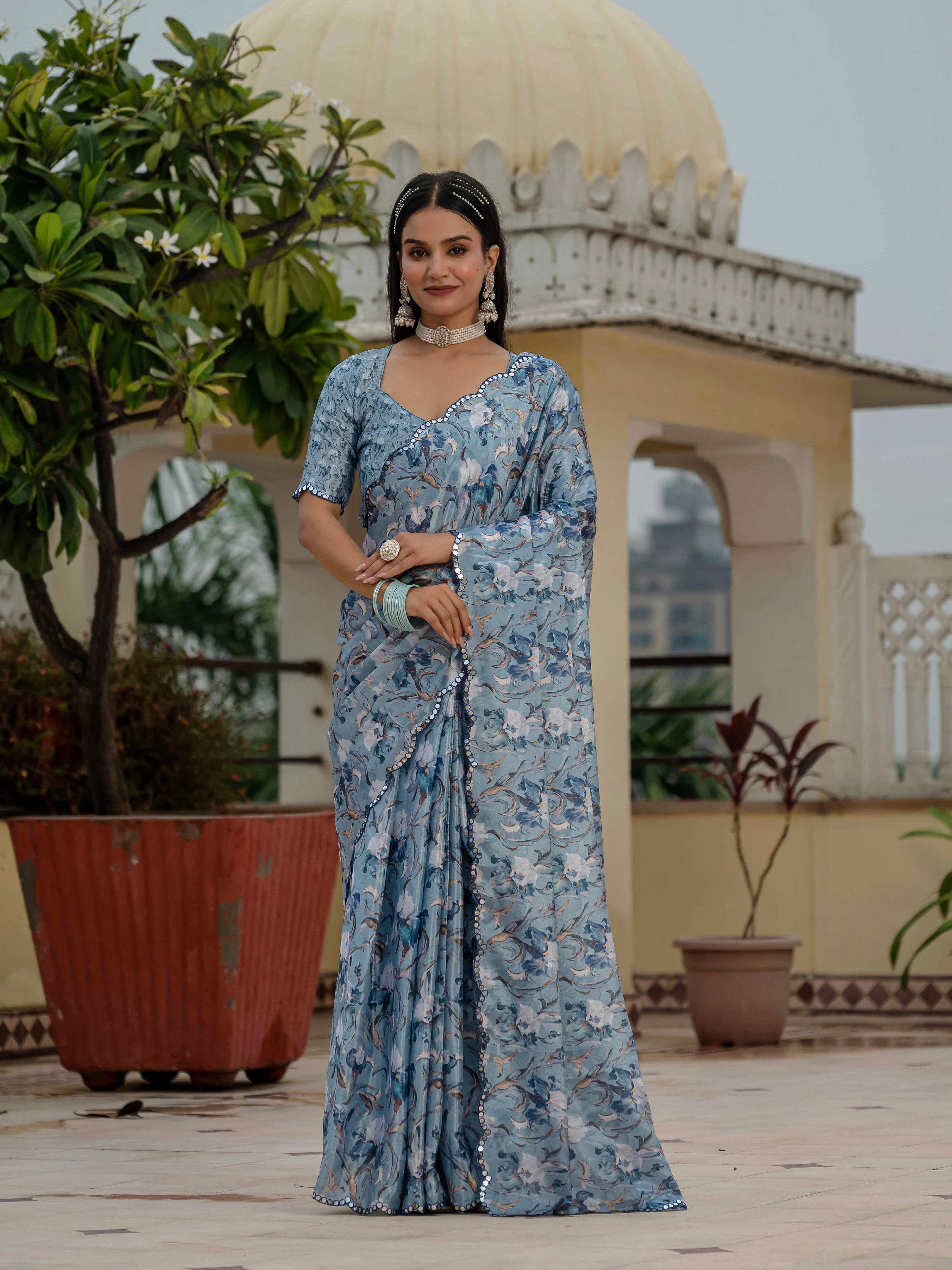 Woman in a blue ready to wear saree standing on a rooftop with plants and architectural elements in the background