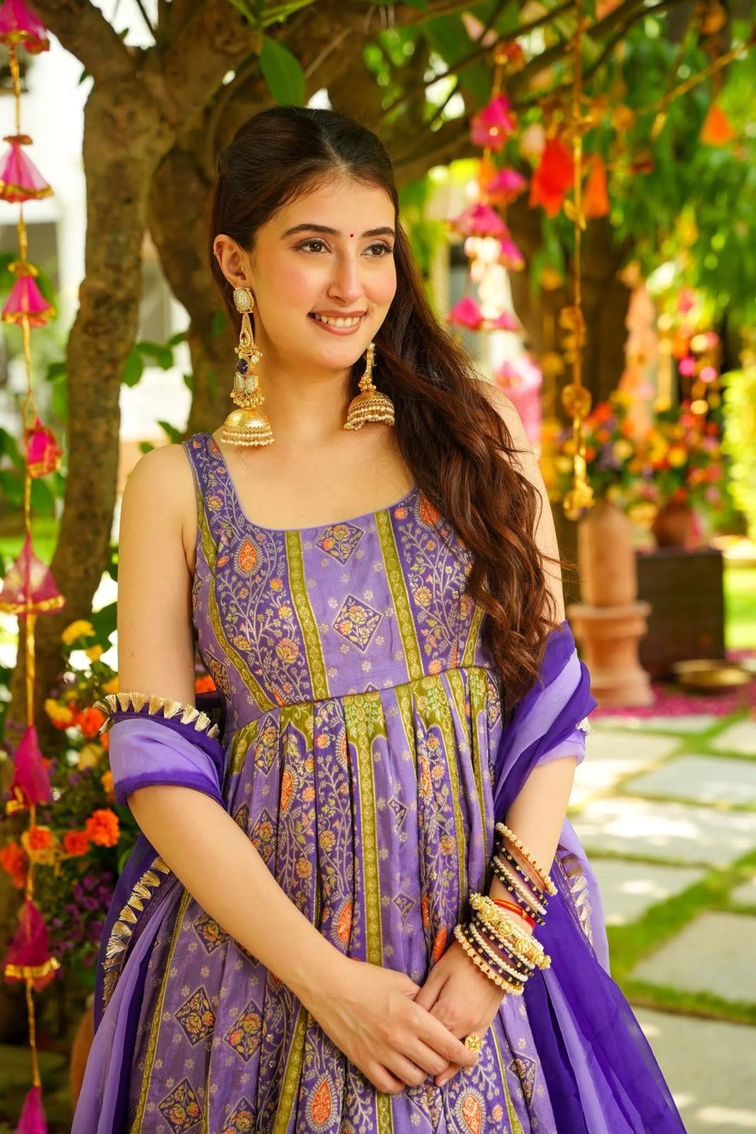 Woman in a purple Anarkali Gown outfit with floral decorations in the background