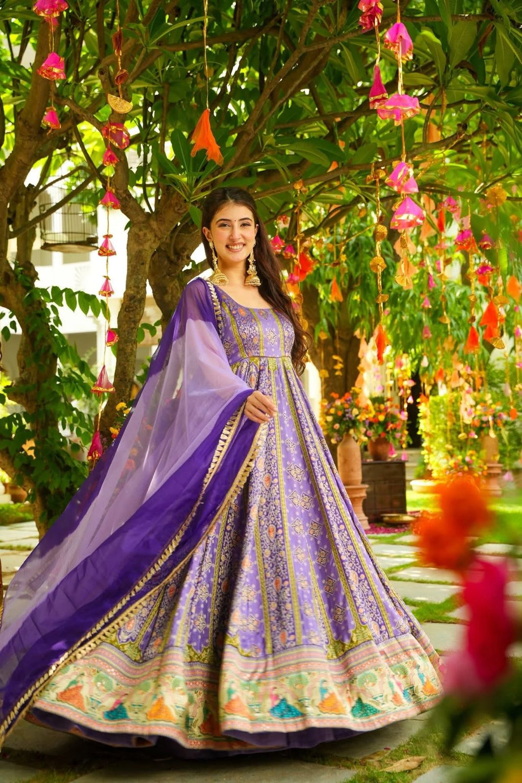 Woman in a Anarkali Gown outfit standing in a decorated garden with hanging flowers.