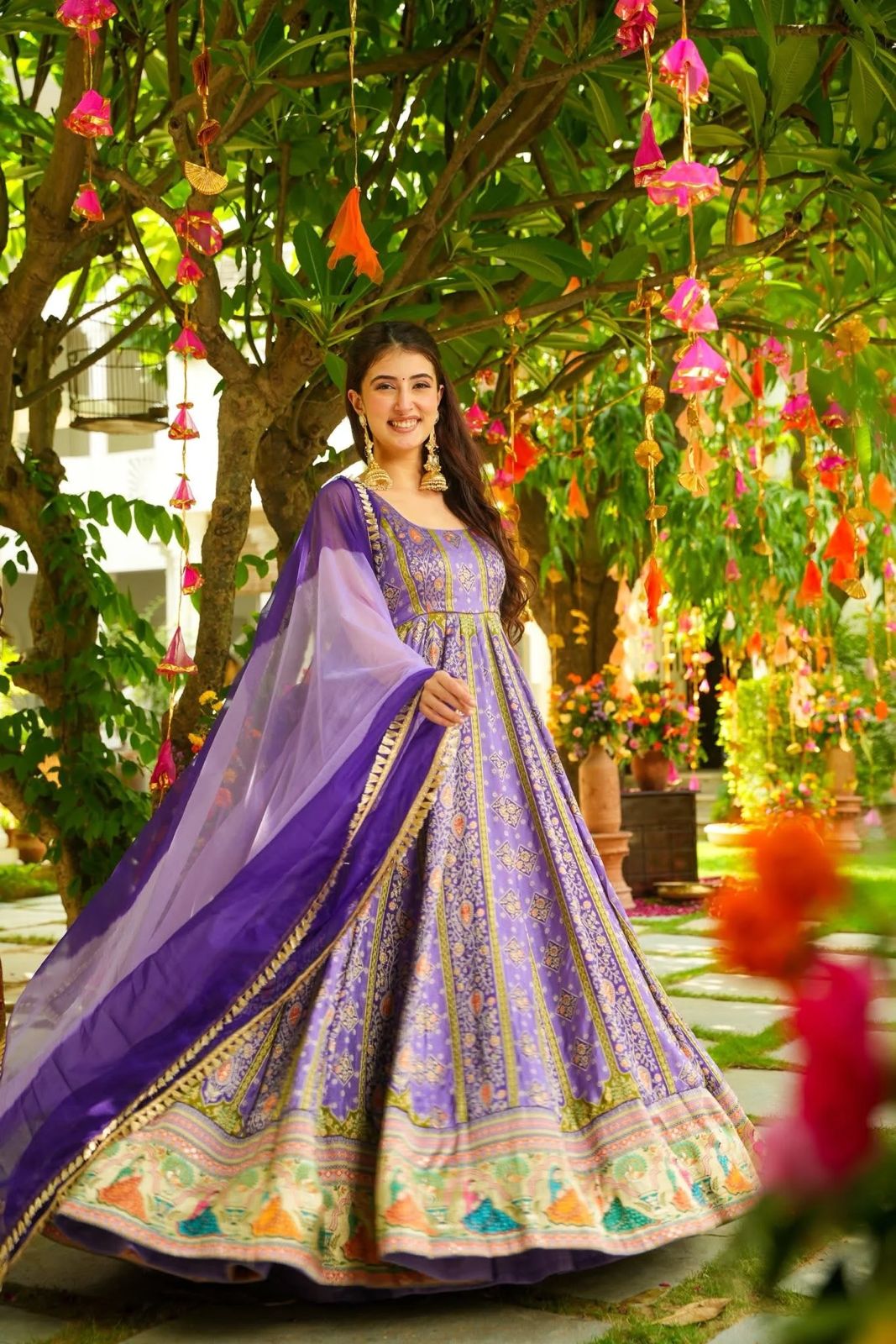 Woman in a Anarkali Gown outfit standing in a decorated garden with hanging flowers.