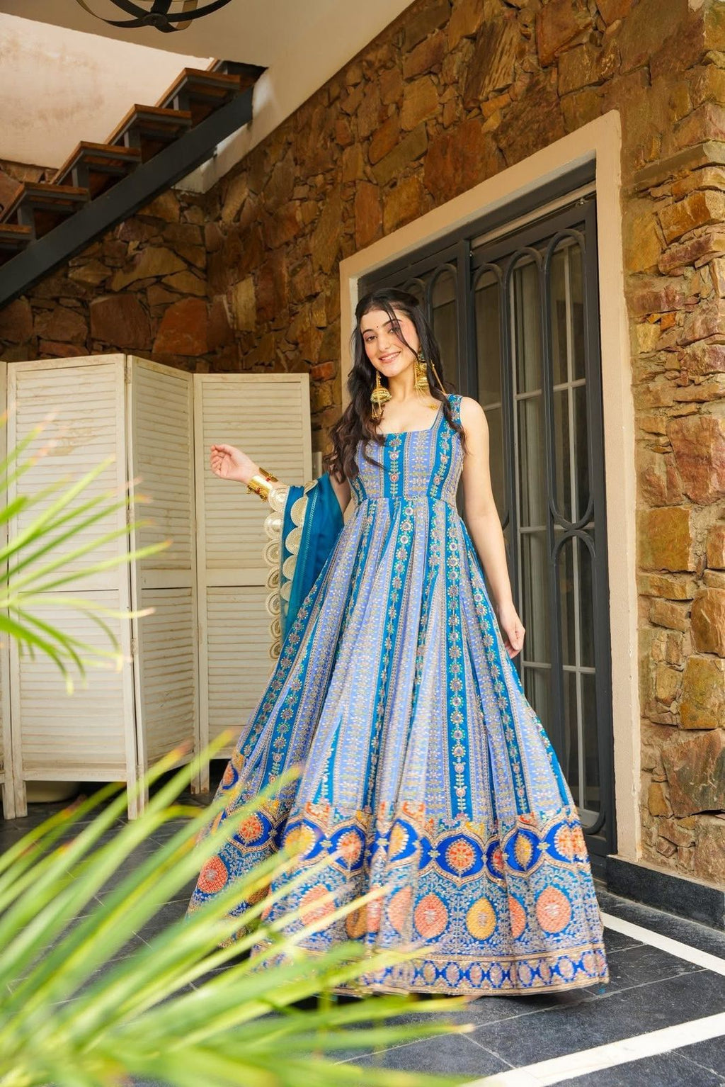 Woman in a blue patterned Anarkali Gown standing in front of a stone wall.