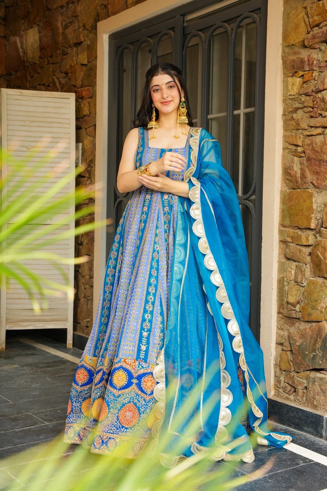 Woman in a blue Anarkali Gown standing in front of a stone wall.