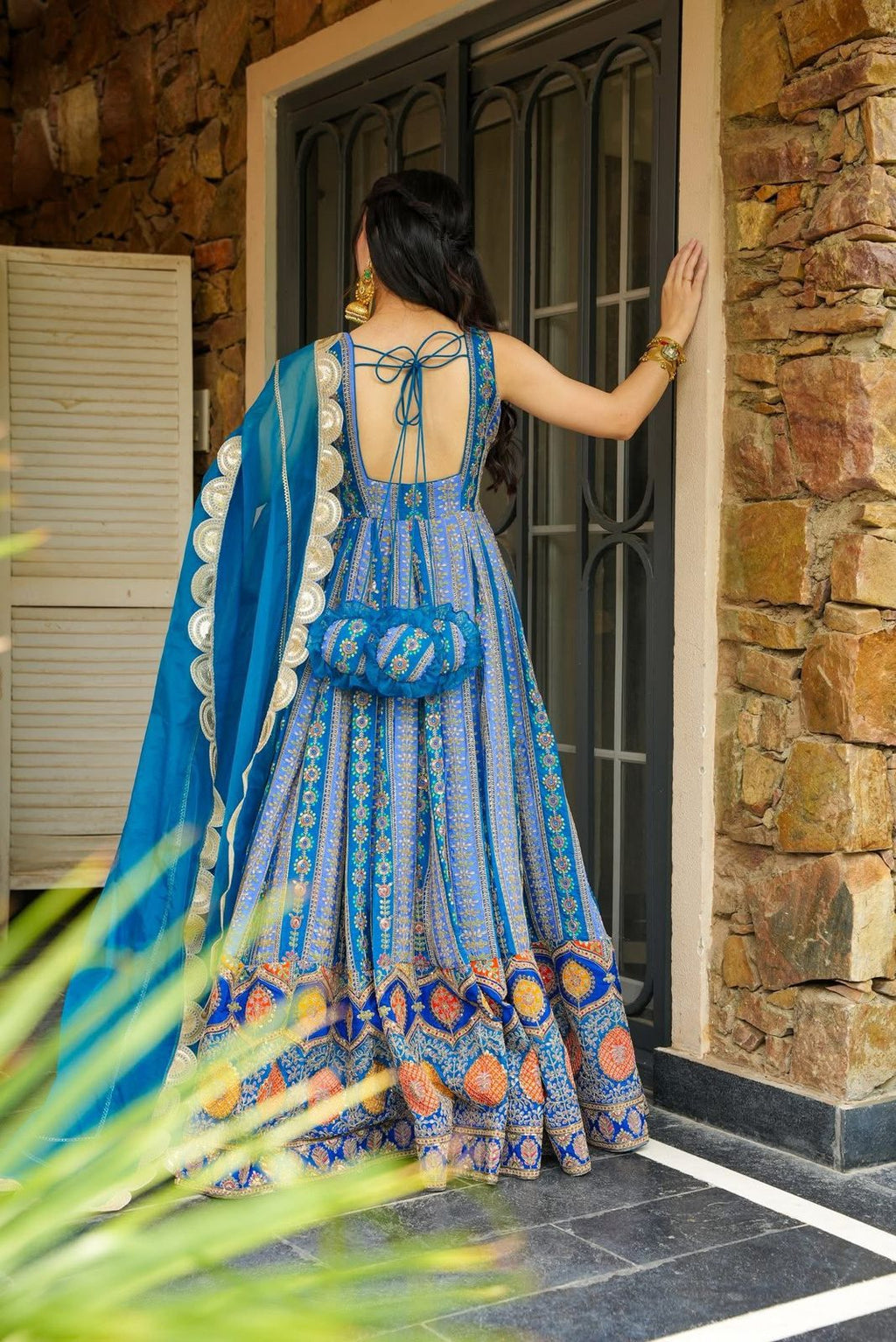 Woman in a blue patterned Anarkali Gown standing in front of a stone wall.
