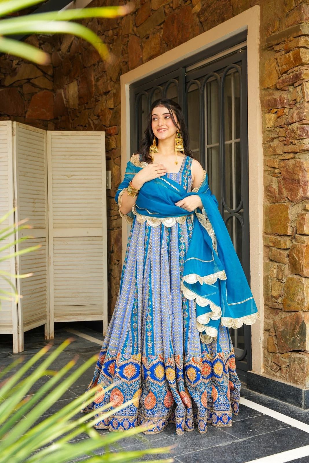 Woman in a blue Anarkali Gown outfit standing in front of a stone wall.