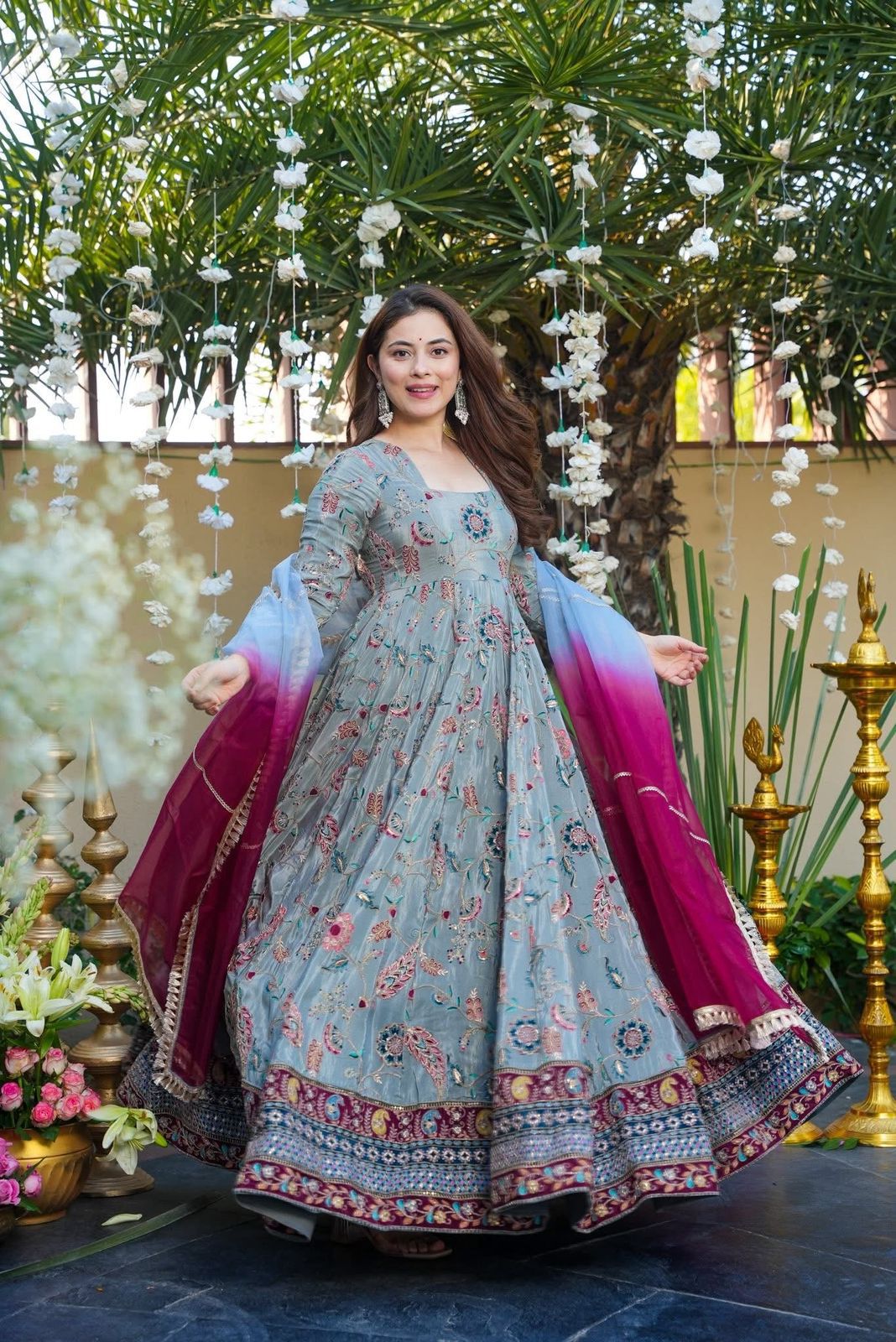 Woman in a Anarkali Gown outfit with a floral design standing in a decorated outdoor setting.