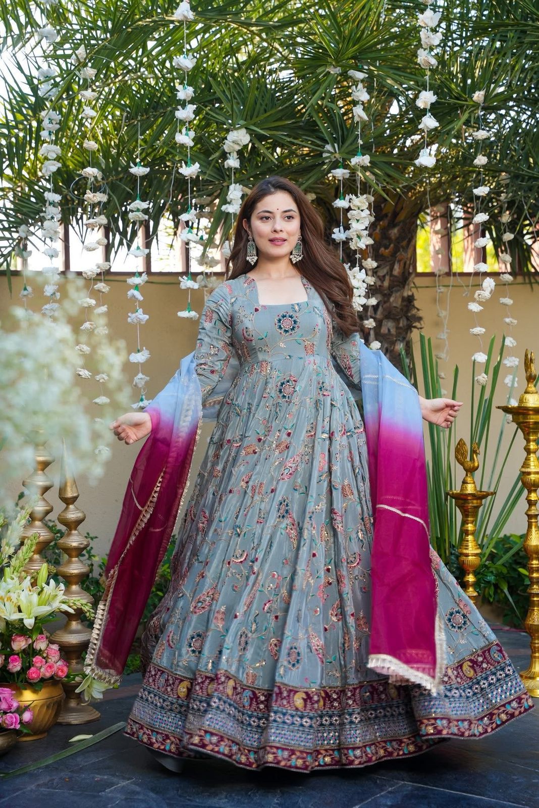 Woman in a Anarkali Gown outfit with floral patterns standing outdoors with decorative elements.