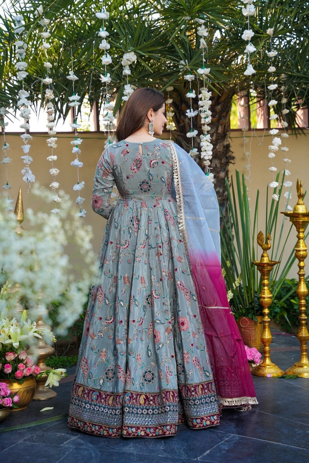 Woman in a Anarkali Gown outfit with floral patterns in an outdoor setting with decorations.