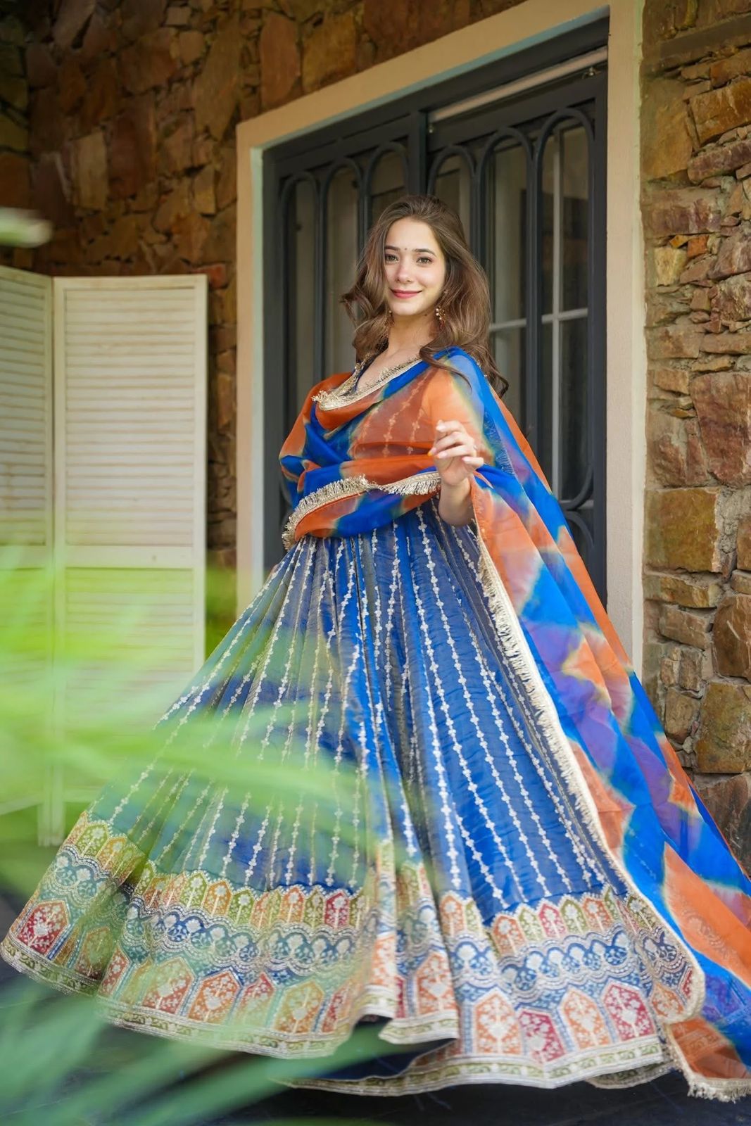 Woman in a traditional blue and orange Anarkali Gown standing outdoors.
