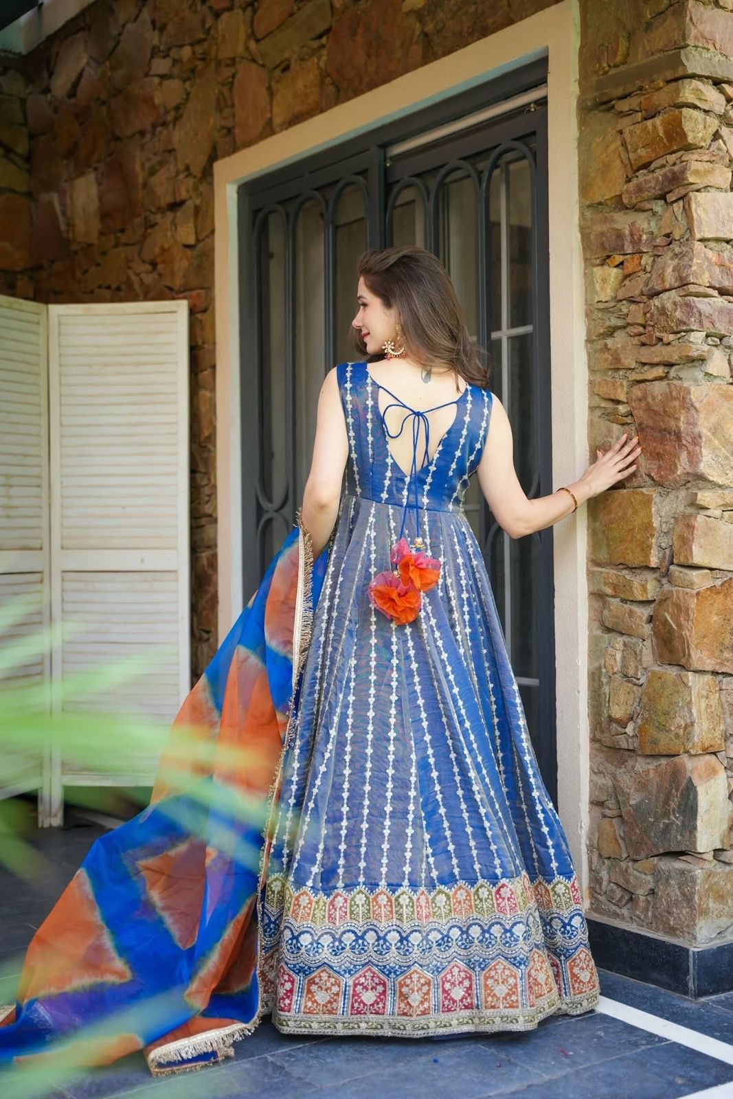 Woman in a blue patterned Anarkali Gown standing in front of a stone wall.