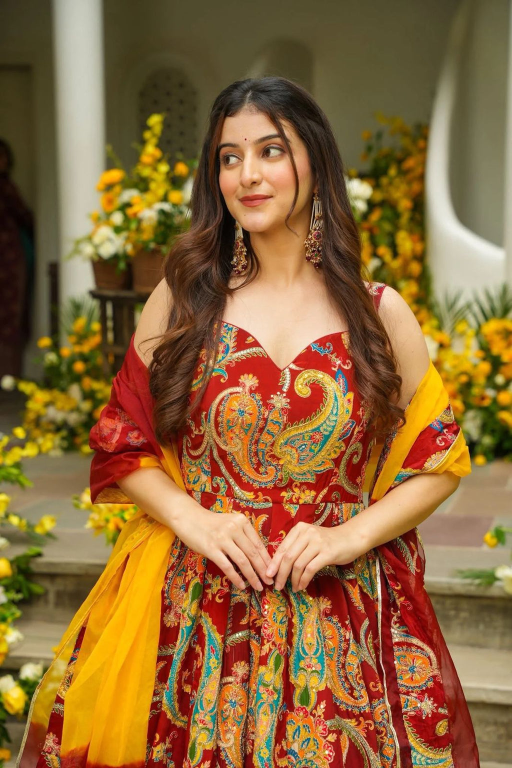 Woman in a colorful traditional Anarkali Gown standing in front of floral decorations.