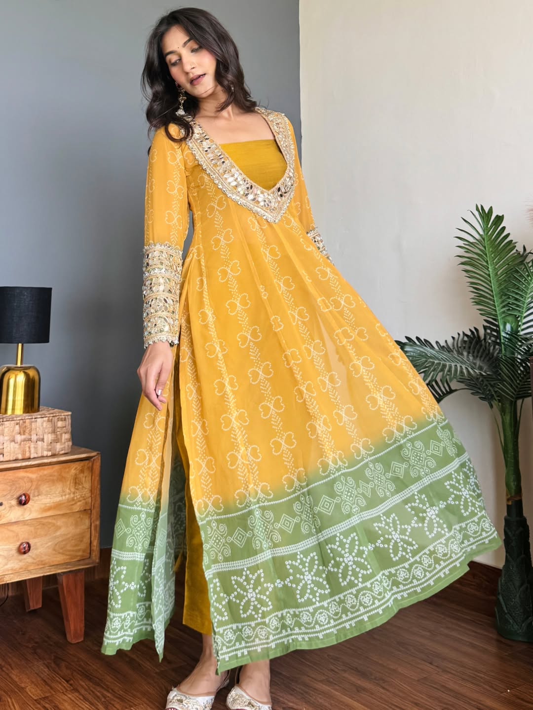 Woman wearing a yellow and green traditional Anarkali Kurta Set outfit with intricate patterns in a room.