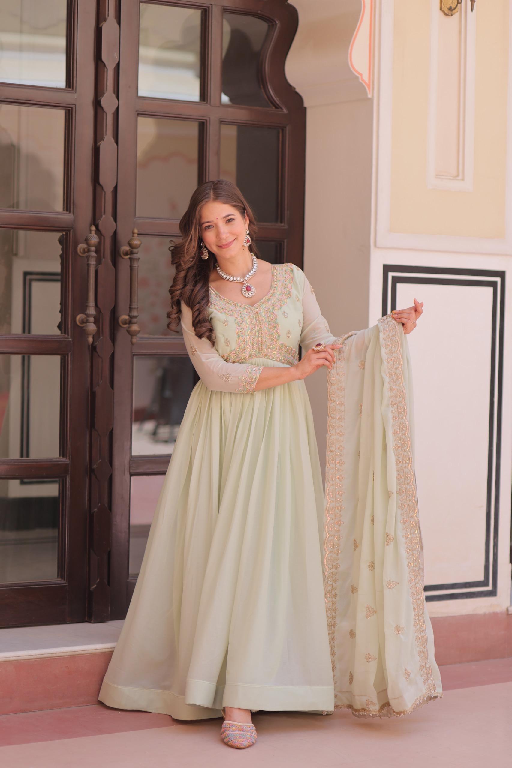 A woman in a light green Anarkali gown or dress holding a dupatta in an indoor setting.