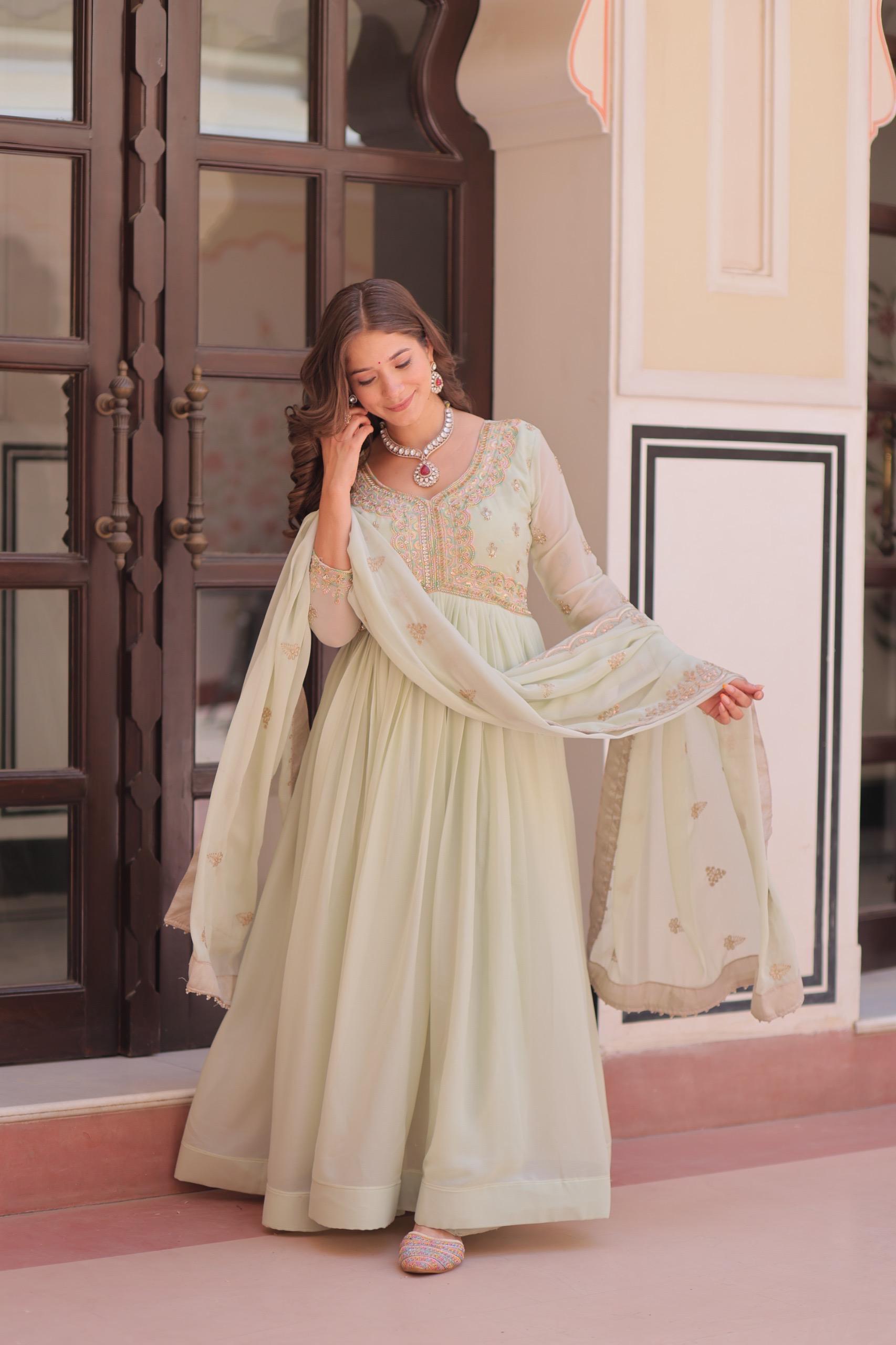 A Woman in a light green Anarkali gown or dress standing in front of a decorative door.