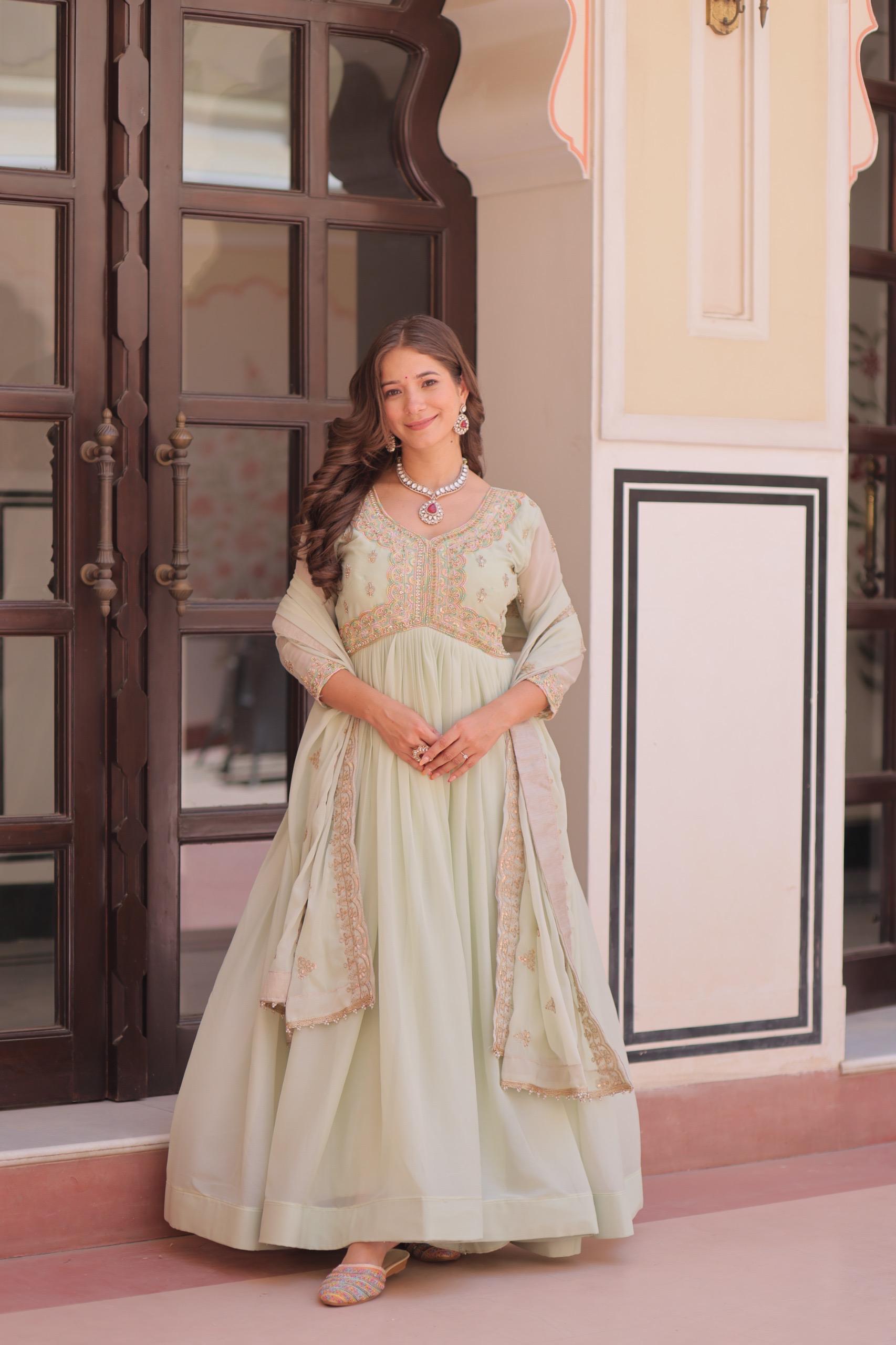A woman in a light green Anarkali gown or dress standing in front of a decorative door.