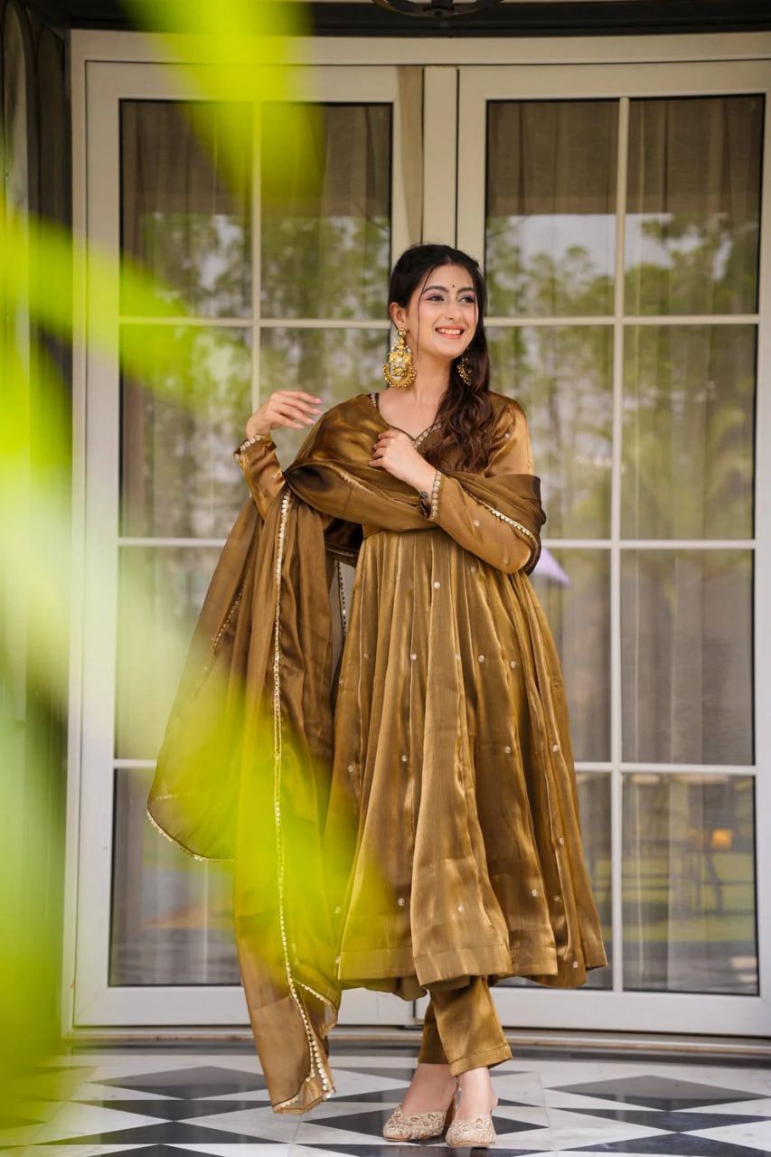 A Woman in a Anarkali gown or dress standing in front of a glass door with a blurred background