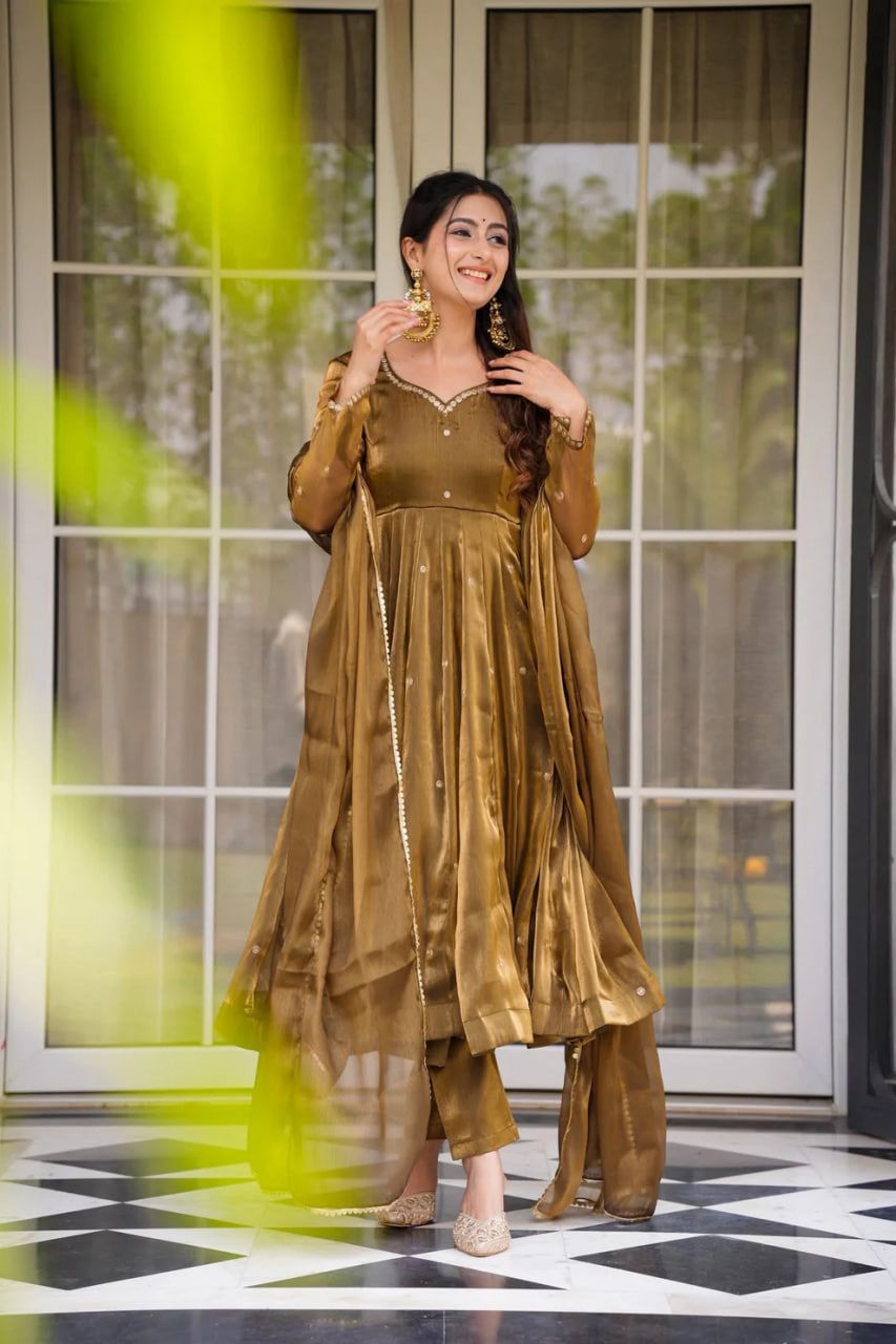 A Woman in a Gold Anarkali gown or dress  standing in front of a glass door with a checkered floor.