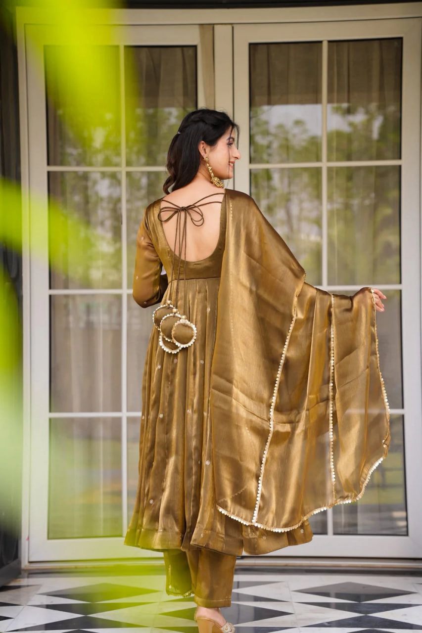 A woman in a brown Anarkali gown or dress standing in front of a glass door.
