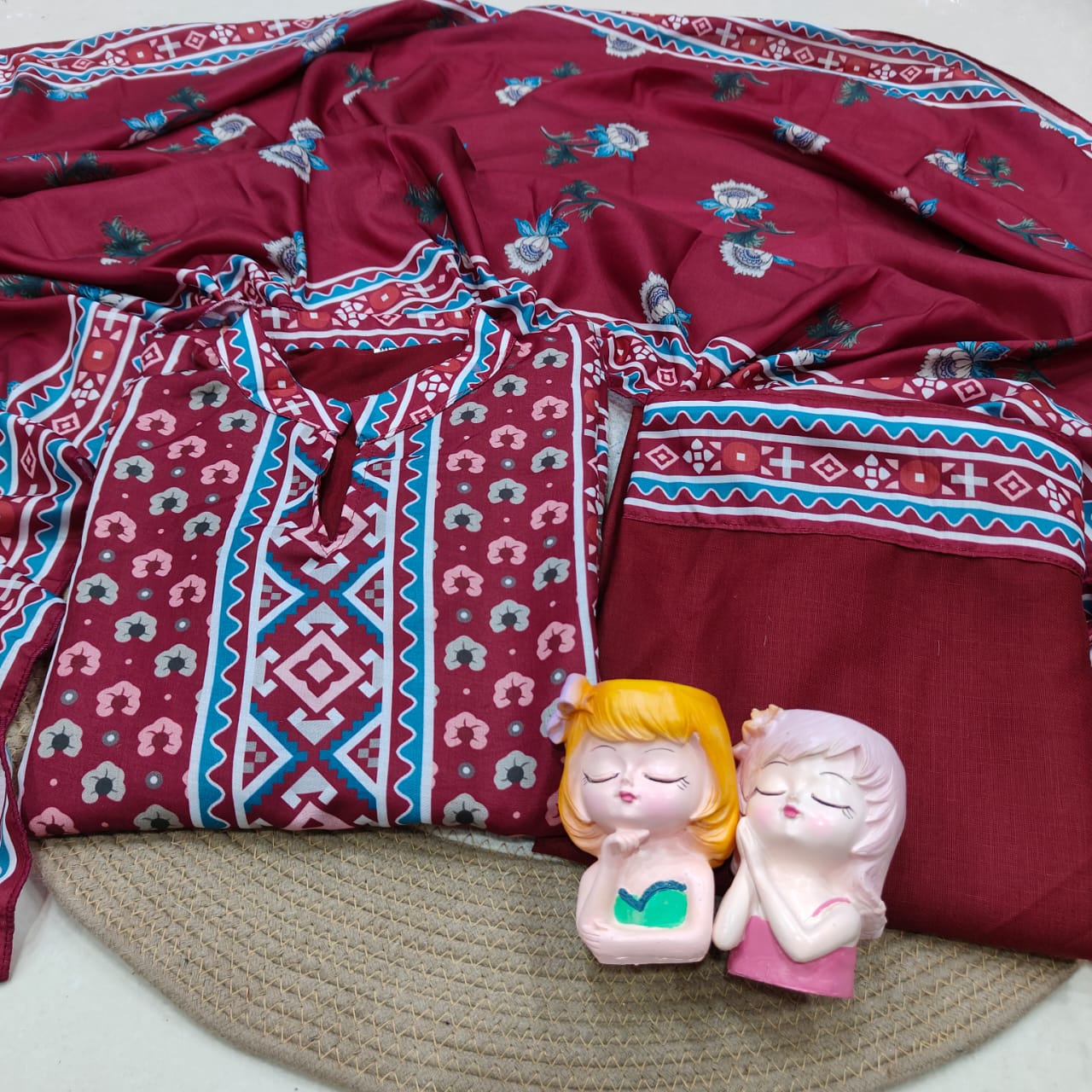 Maroon patterned kurta set dress fabric with two small figurines on a textured surface.