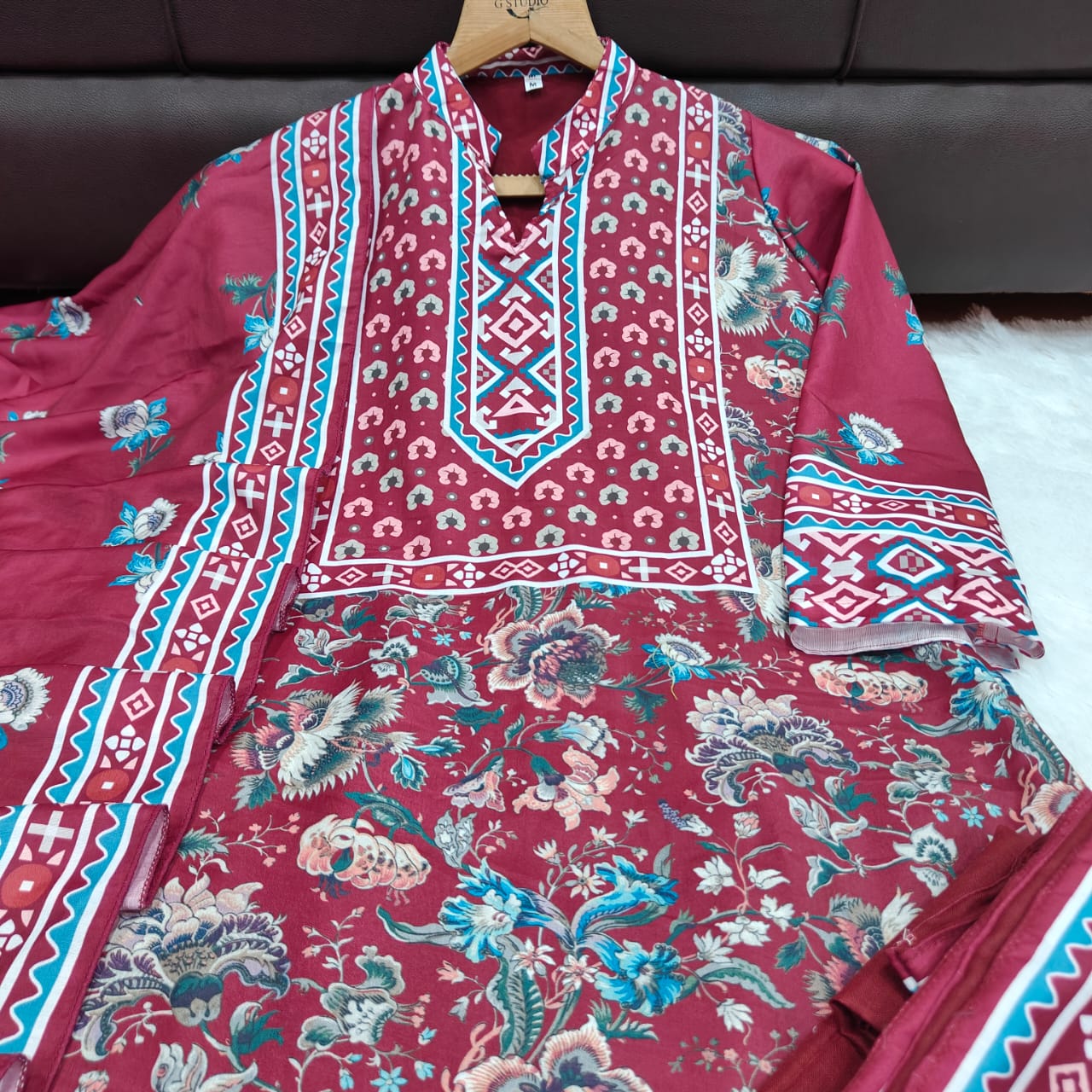 Maroon floral and geometric patterned fabric on a hanger against a dark background