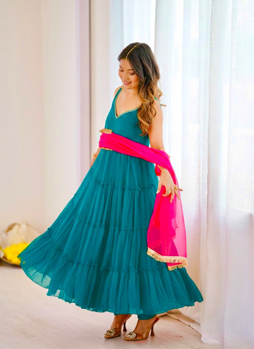 Woman wearing a blue anarkali dress with a pink dupatta in a bright room.