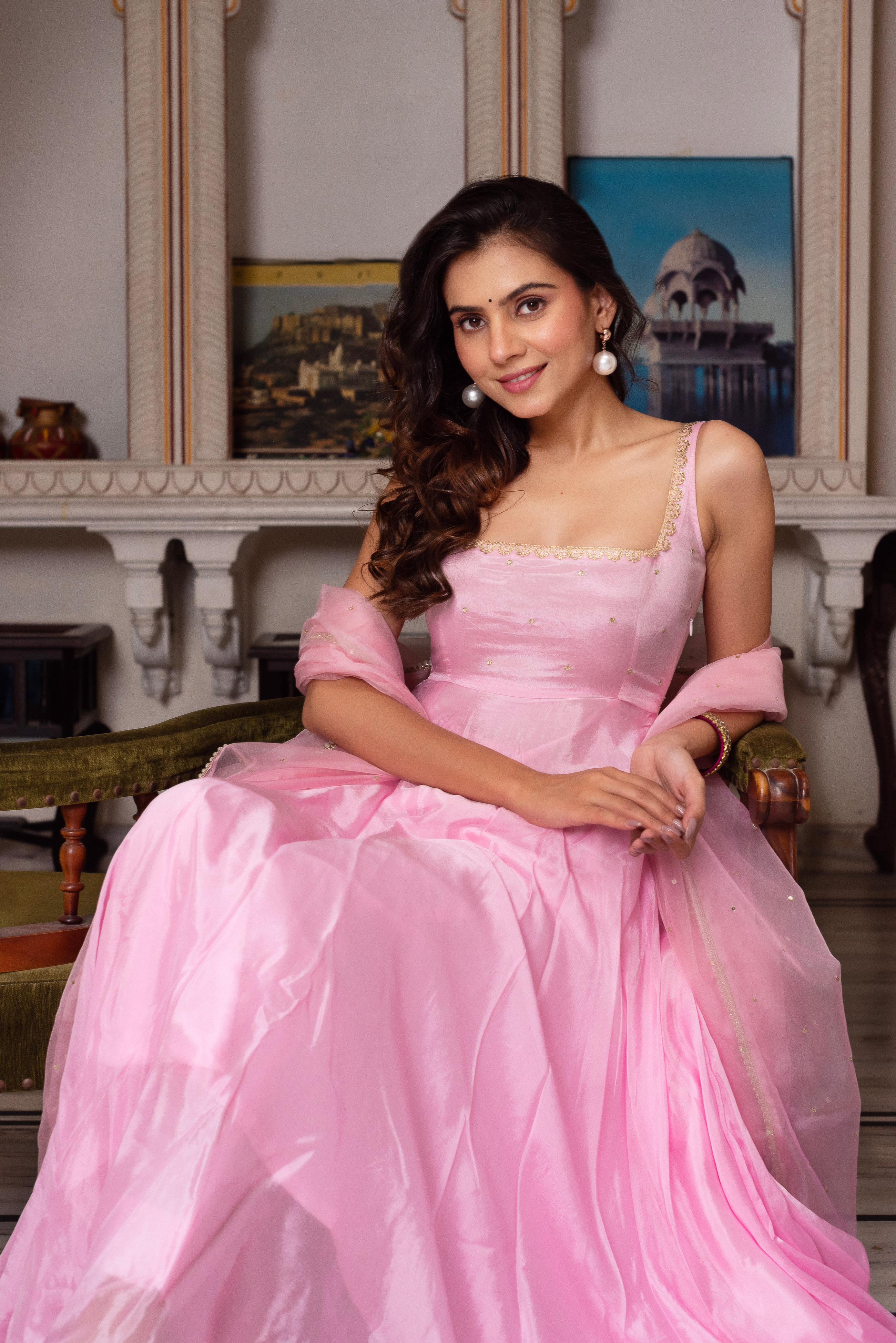 Woman in a pink dress sitting in an elegant room with decorative elements.