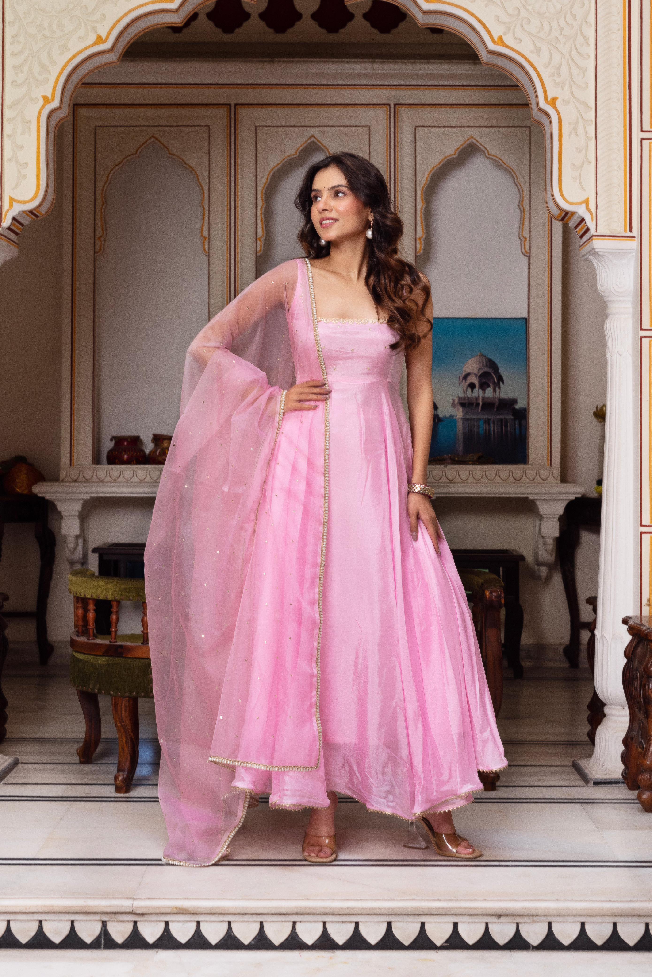 Woman in a pink traditional outfit standing in an ornate room.