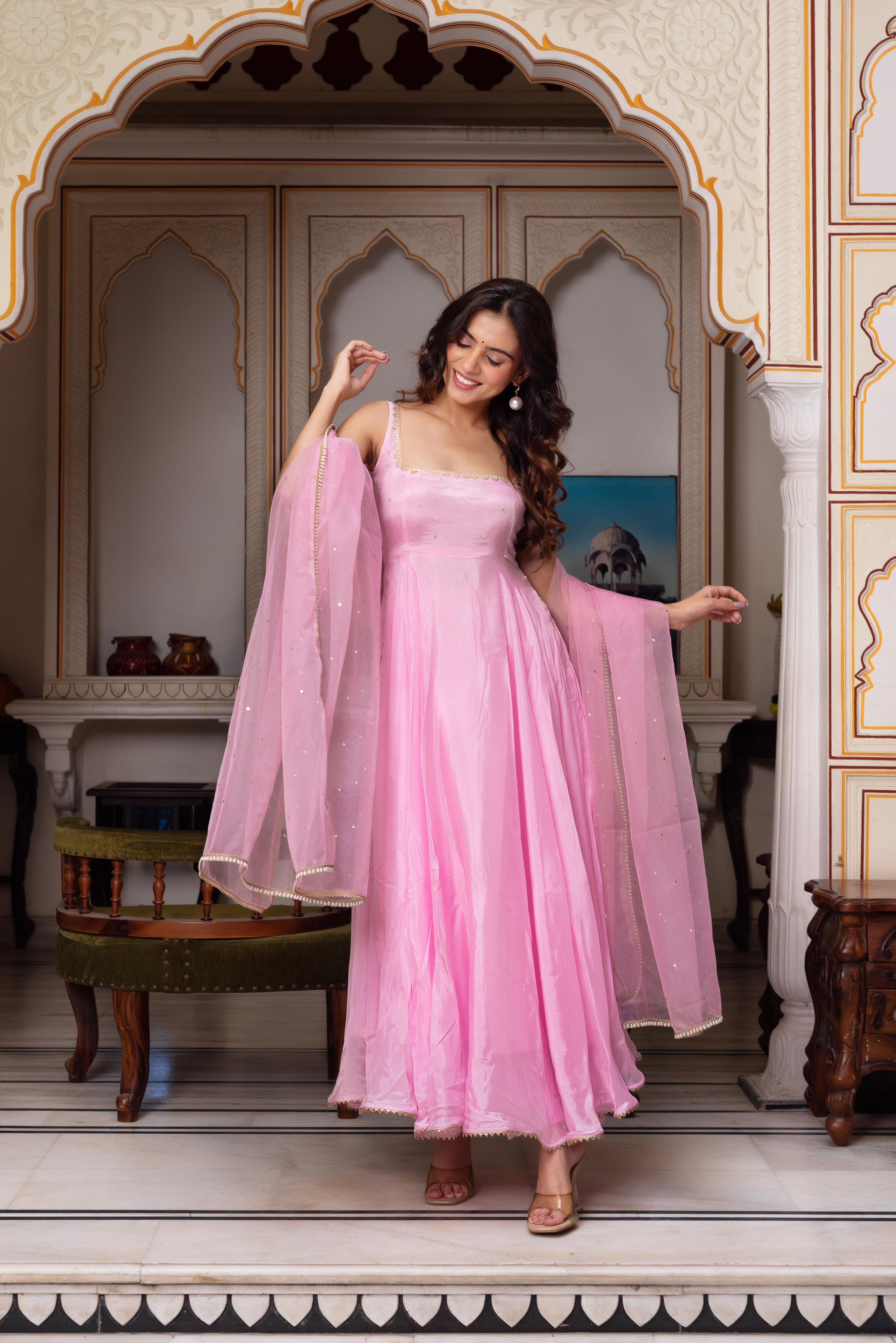 Woman in a pink dress standing in an ornate room with arches.