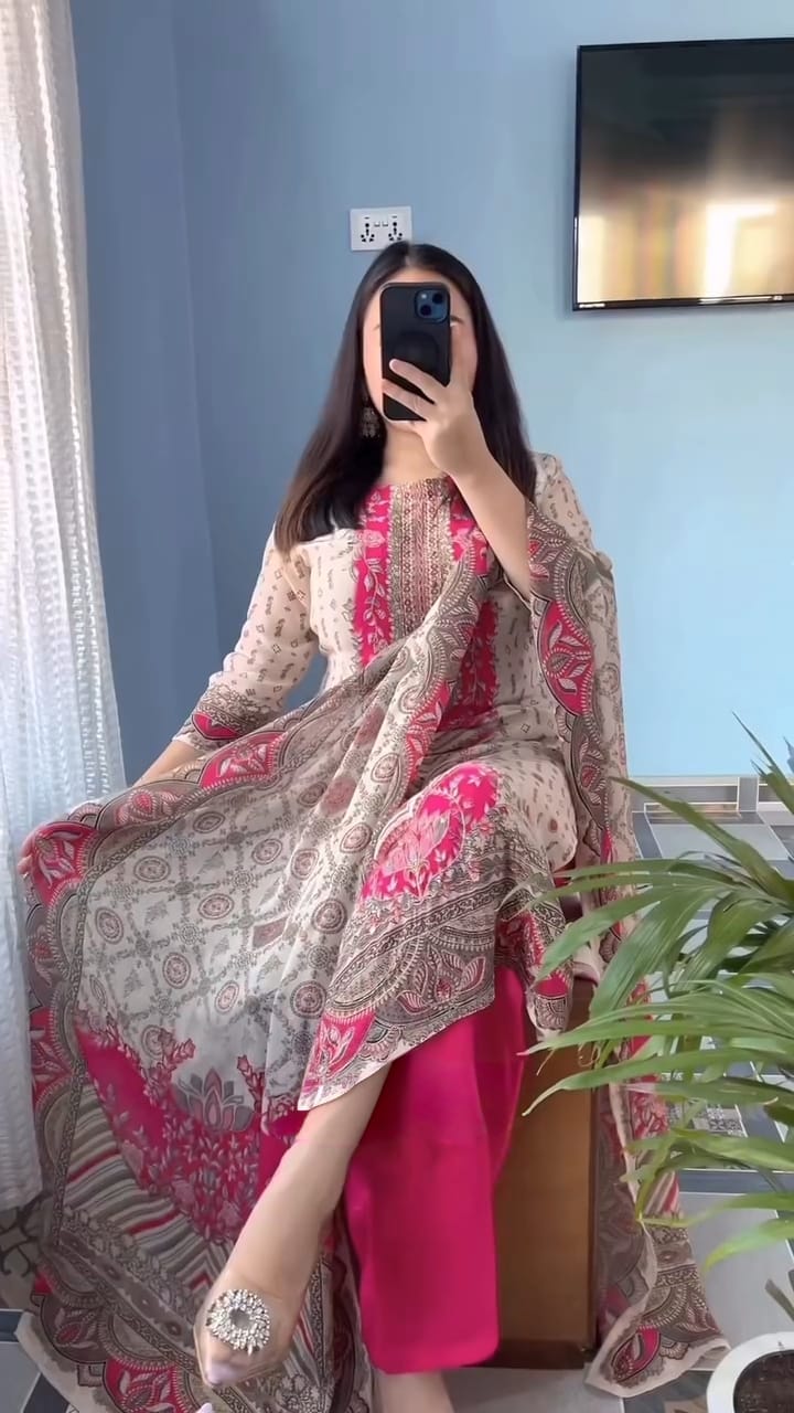 Person wearing a pink and patterned kurta set in a room with a plant and television.