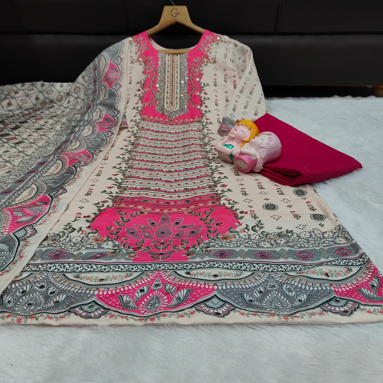 Embroidered traditional kurta set with pink and gray patterns on a white fabric background.