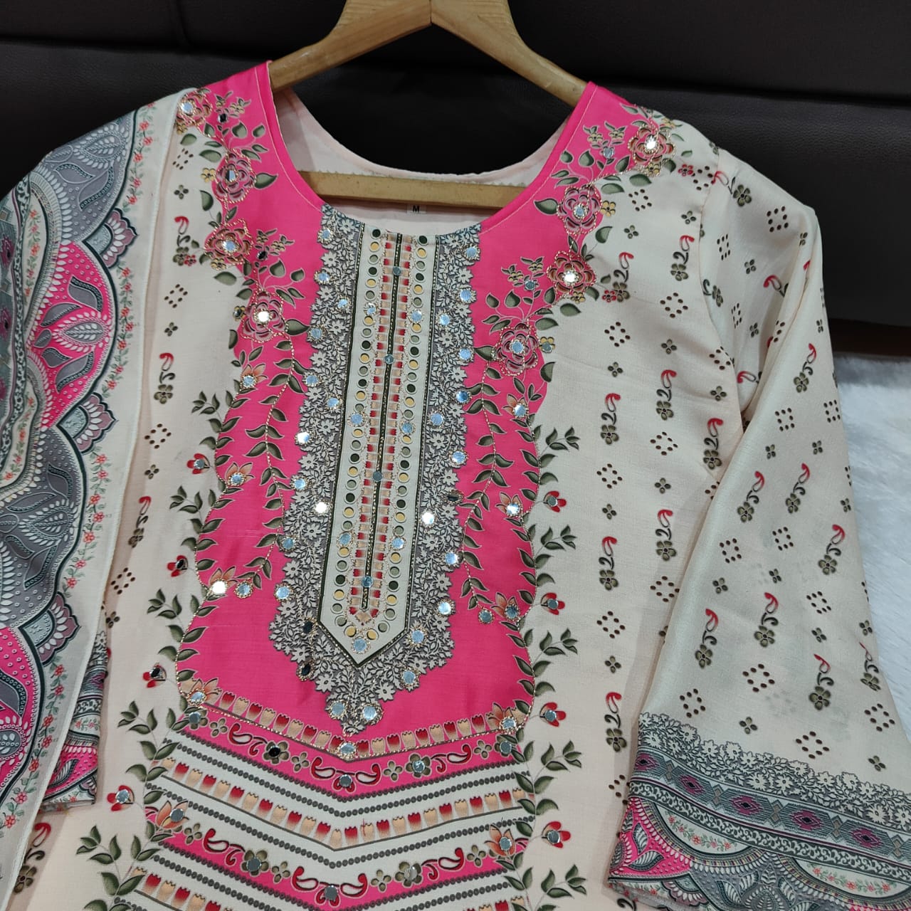 Embroidered garment with pink and silver details on a hanger