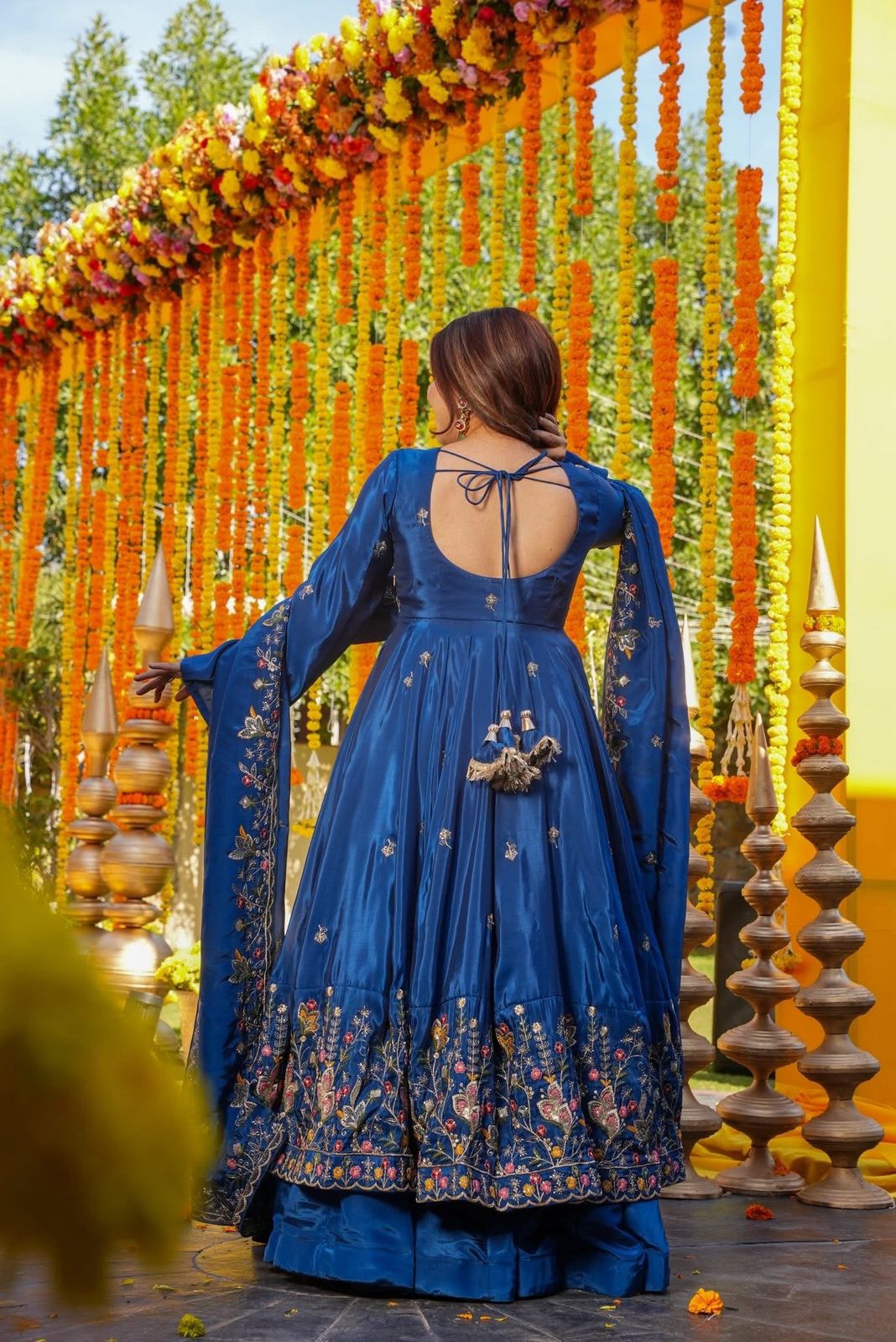 Woman in a blue embroidered dress standing in front of a decorated entrance with flowers and lights.