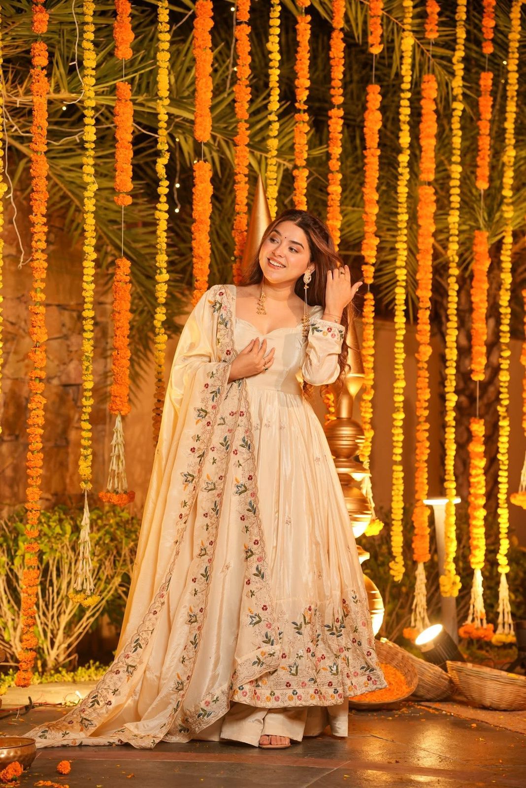 Woman in a traditional outfit standing in front of decorative floral arrangements.