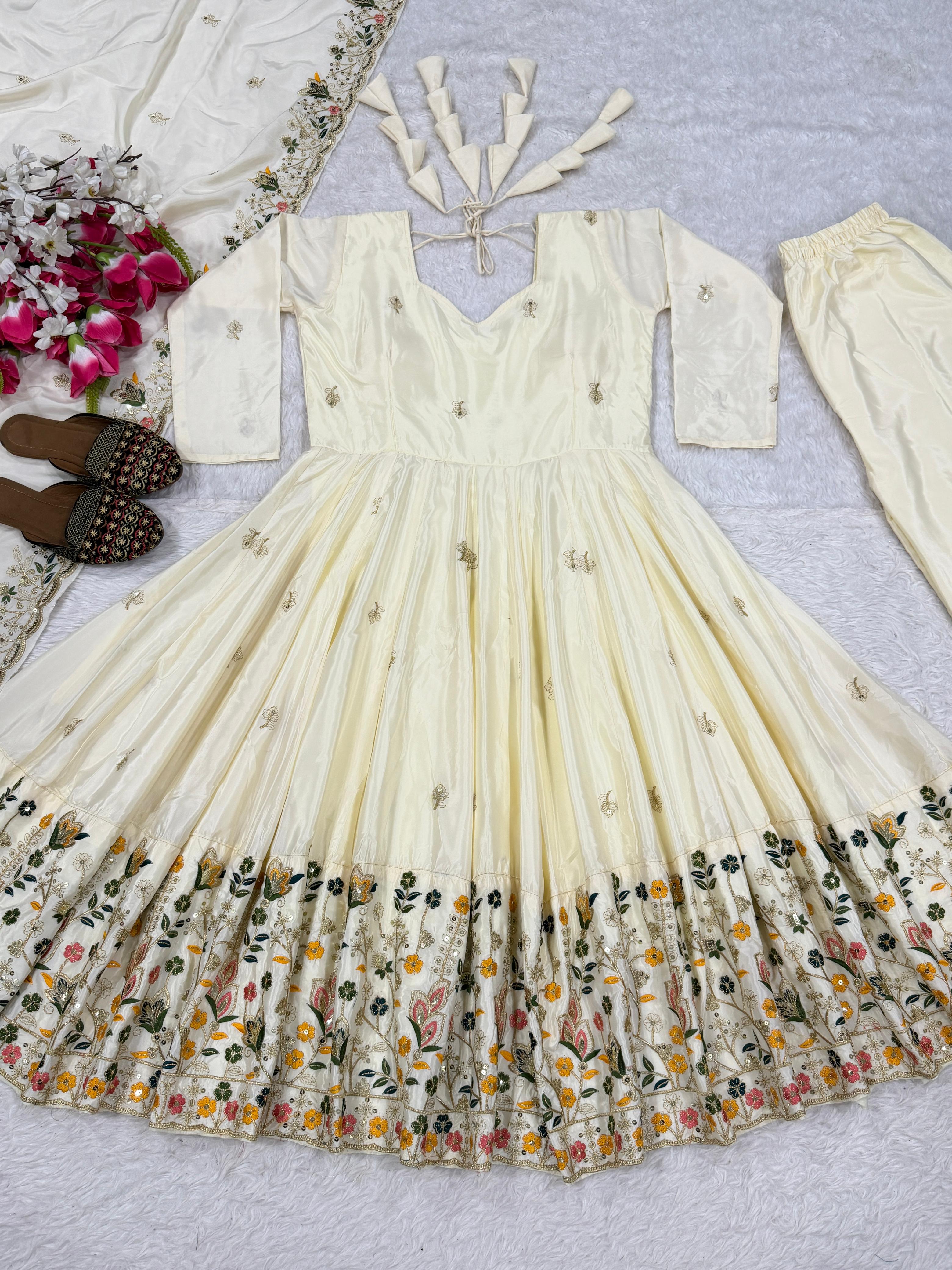 White embroidered dress with floral patterns on a light gray surface, accompanied by a floral arrangement and sandals.