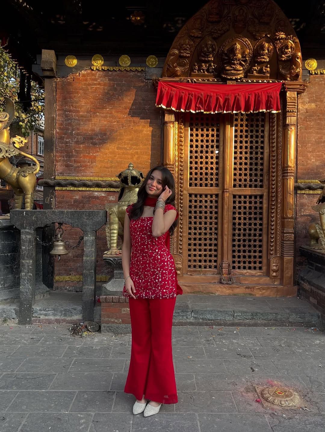 Woman in a red dress standing in front of a traditional wooden door with gold accents and red fabric.