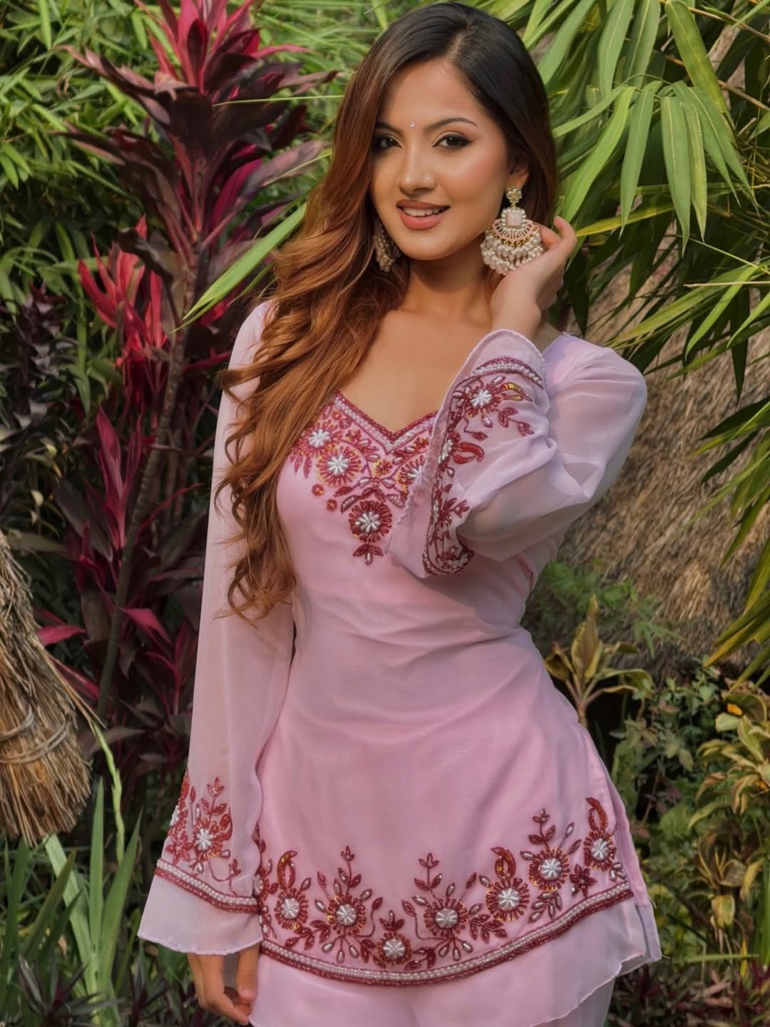 Woman wearing a pink embroidered outfit standing in a garden setting
