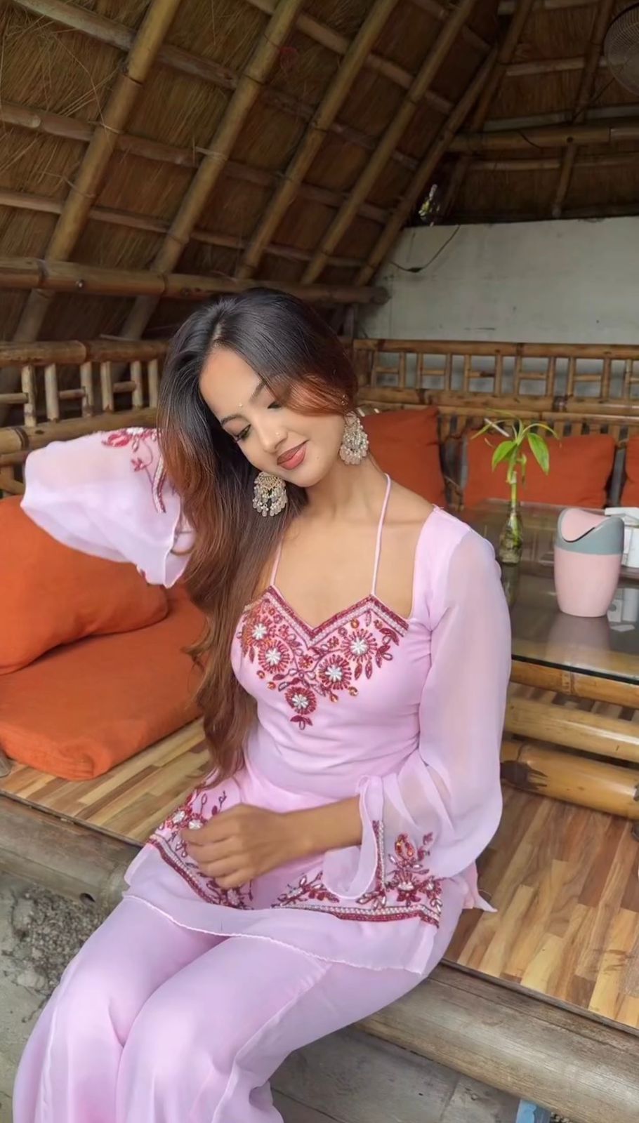 Woman in a pink traditional outfit sitting in a rustic indoor setting.